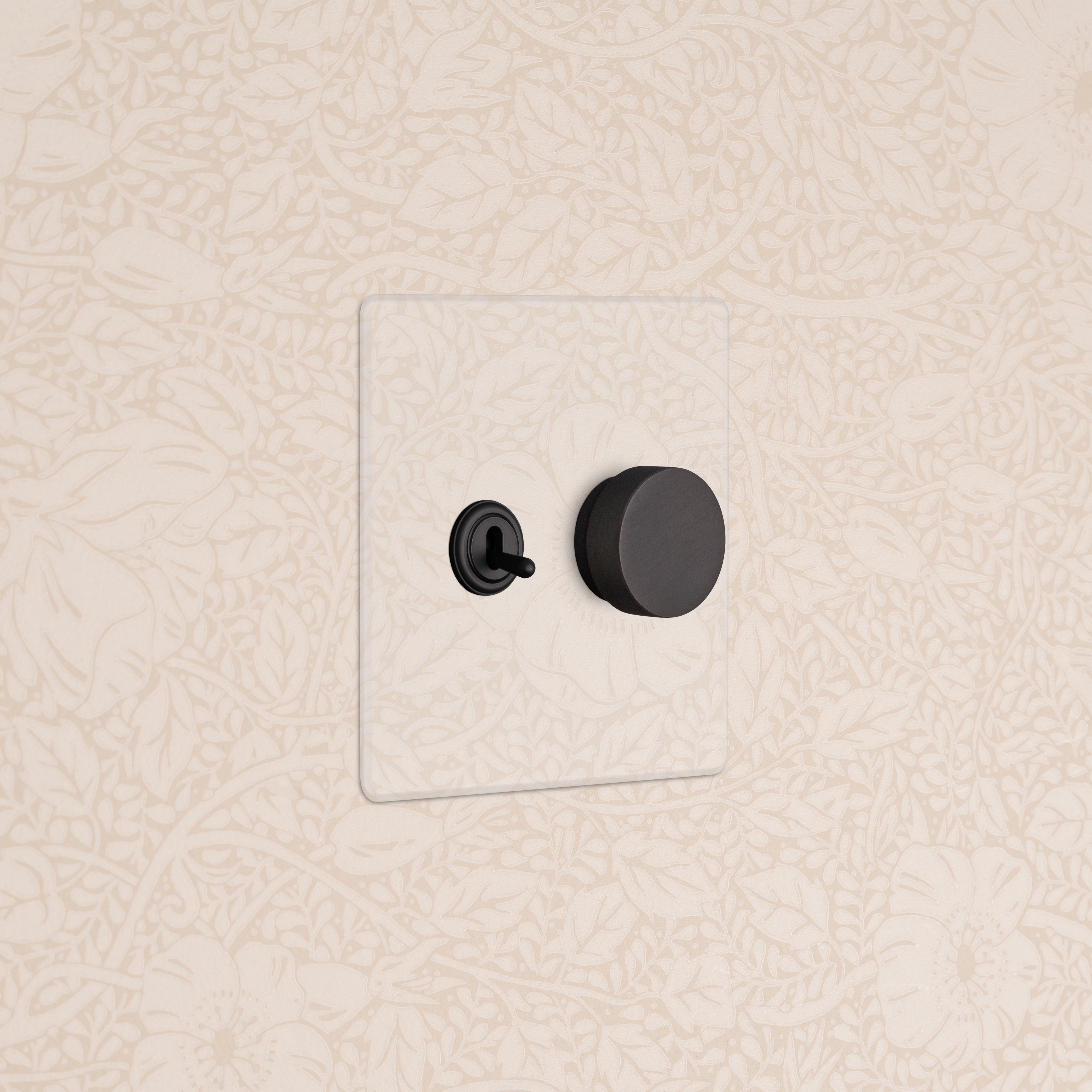 Kew 2G Toggle & Dimmer Switch in clear bronze with black toggle and round dimmer on a beige floral wall.