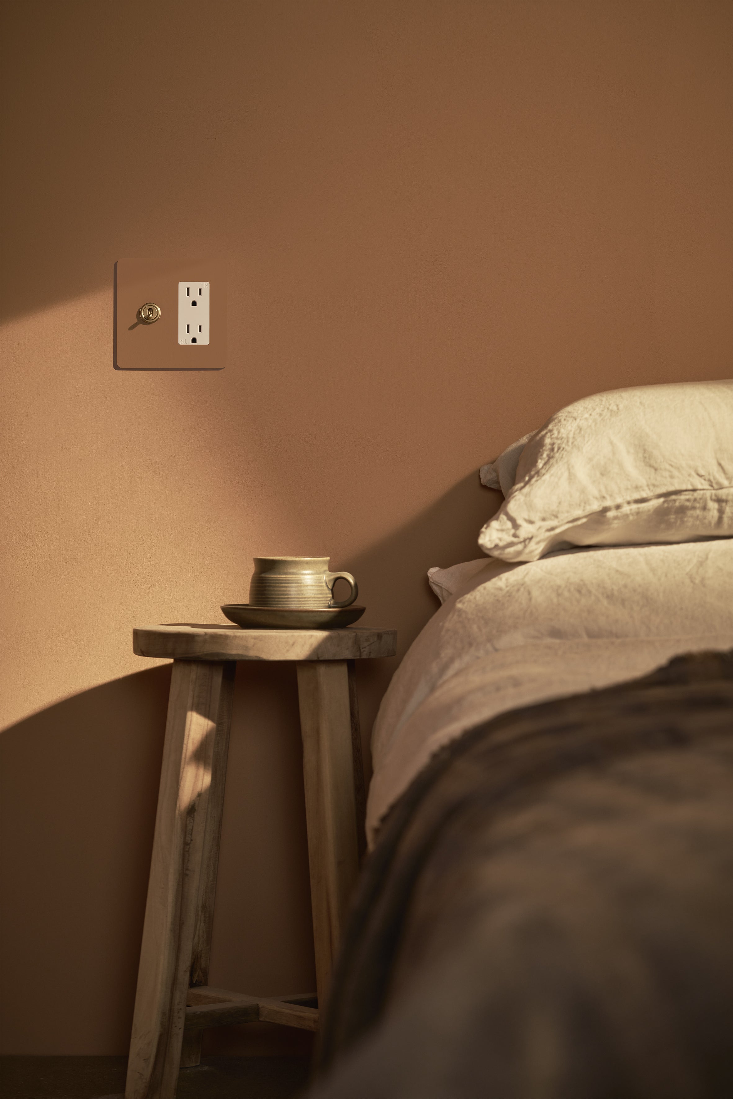 Kew 2G Toggle Switch & Outlet in paintable antique brass white finish mounted on a beige wall.