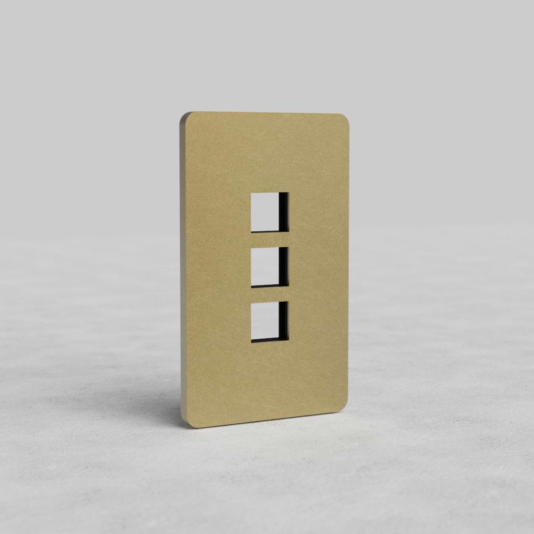 Antique brass 1-gang plate with three vertical keystone openings for Grove US, on a light gray surface.