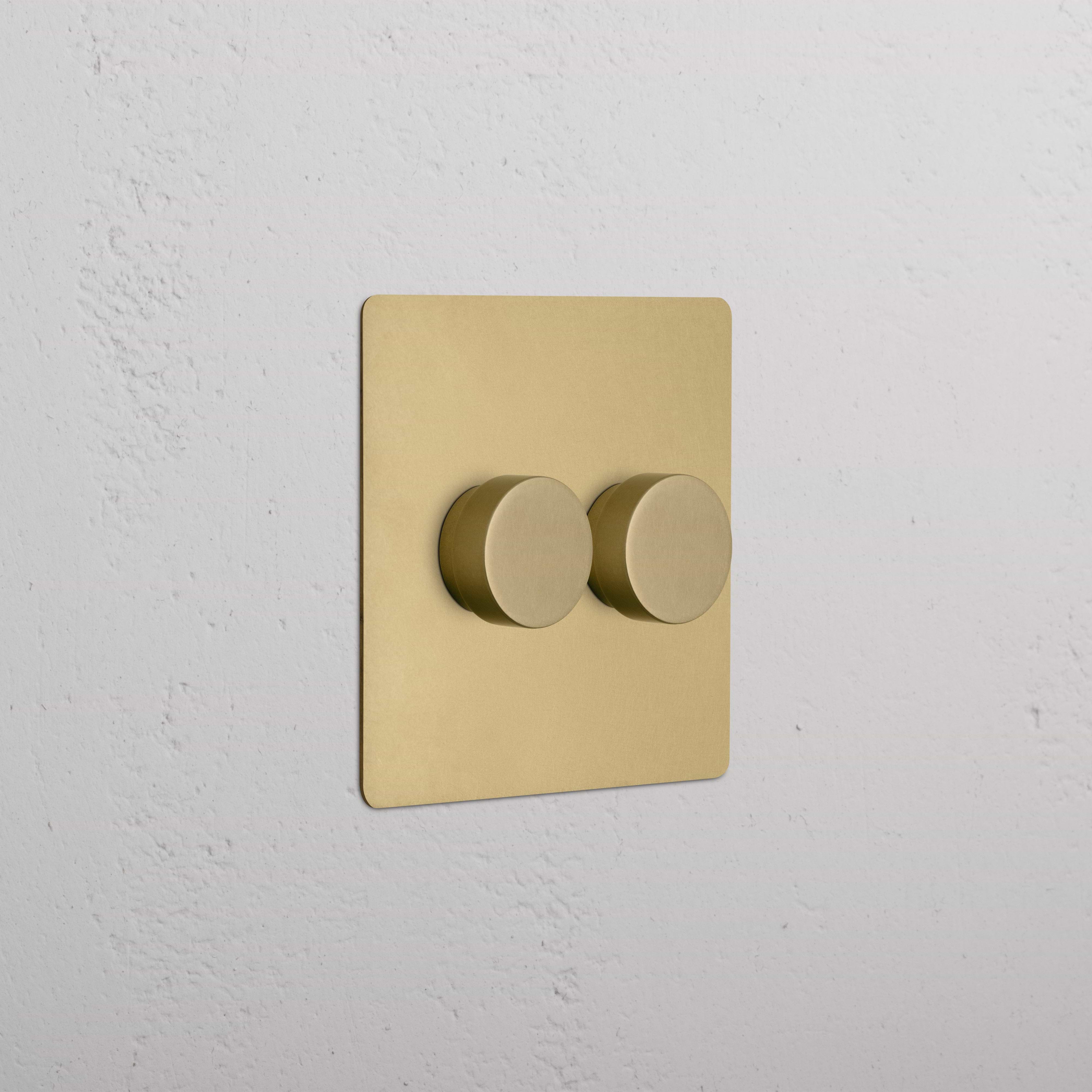 Kew 2G Dimmer Switch in Antique Brass with two round knobs, mounted on a white textured wall.