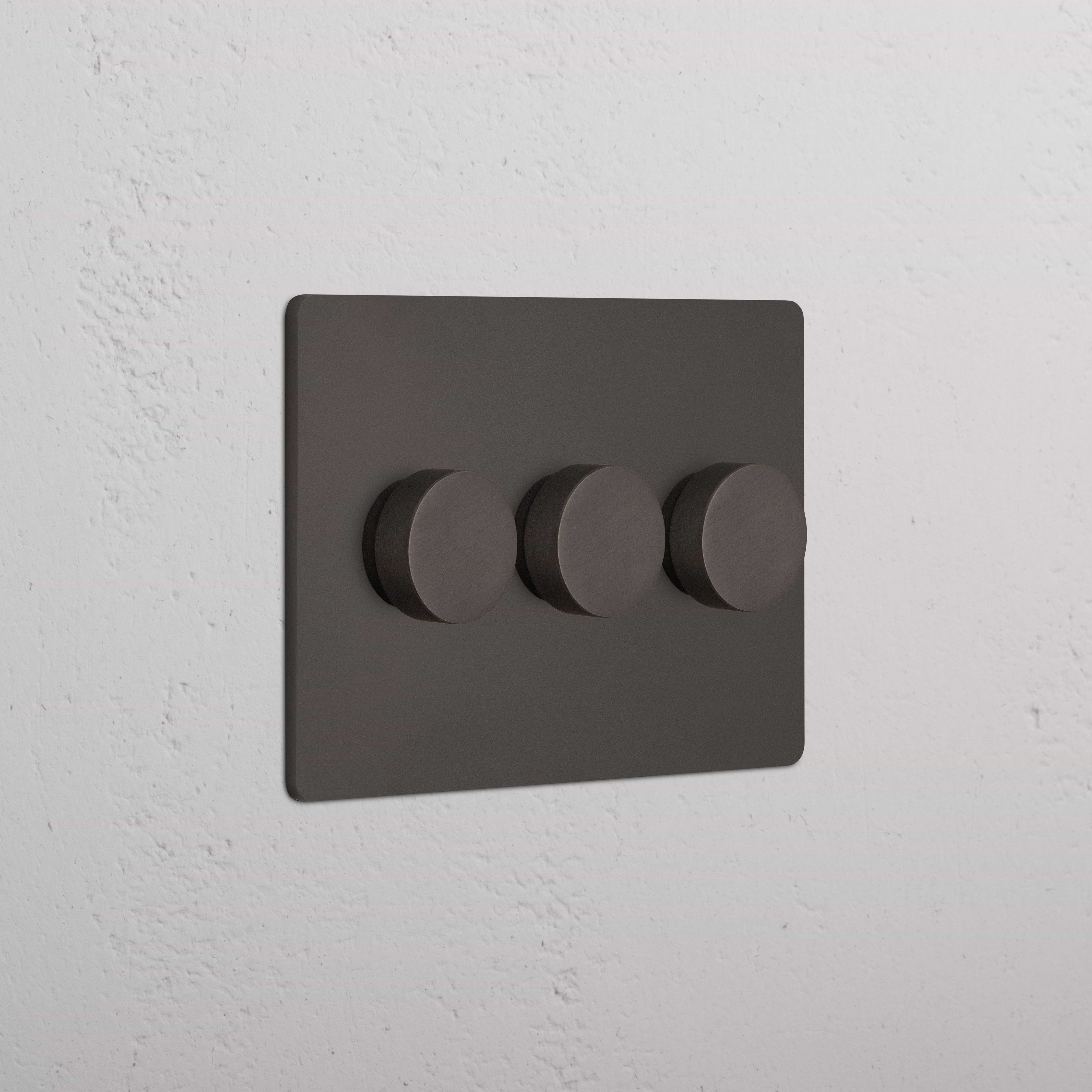 Bronze Grove 3G Dimmer Switch with three round knobs on a rectangular wall plate, mounted on a wall.