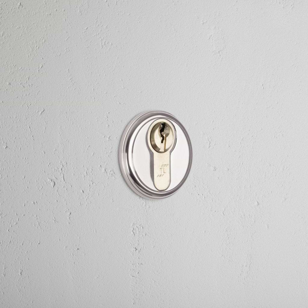 Canning Key Escutcheon in polished nickel, installed on a light gray wall, showing its circular key slot.