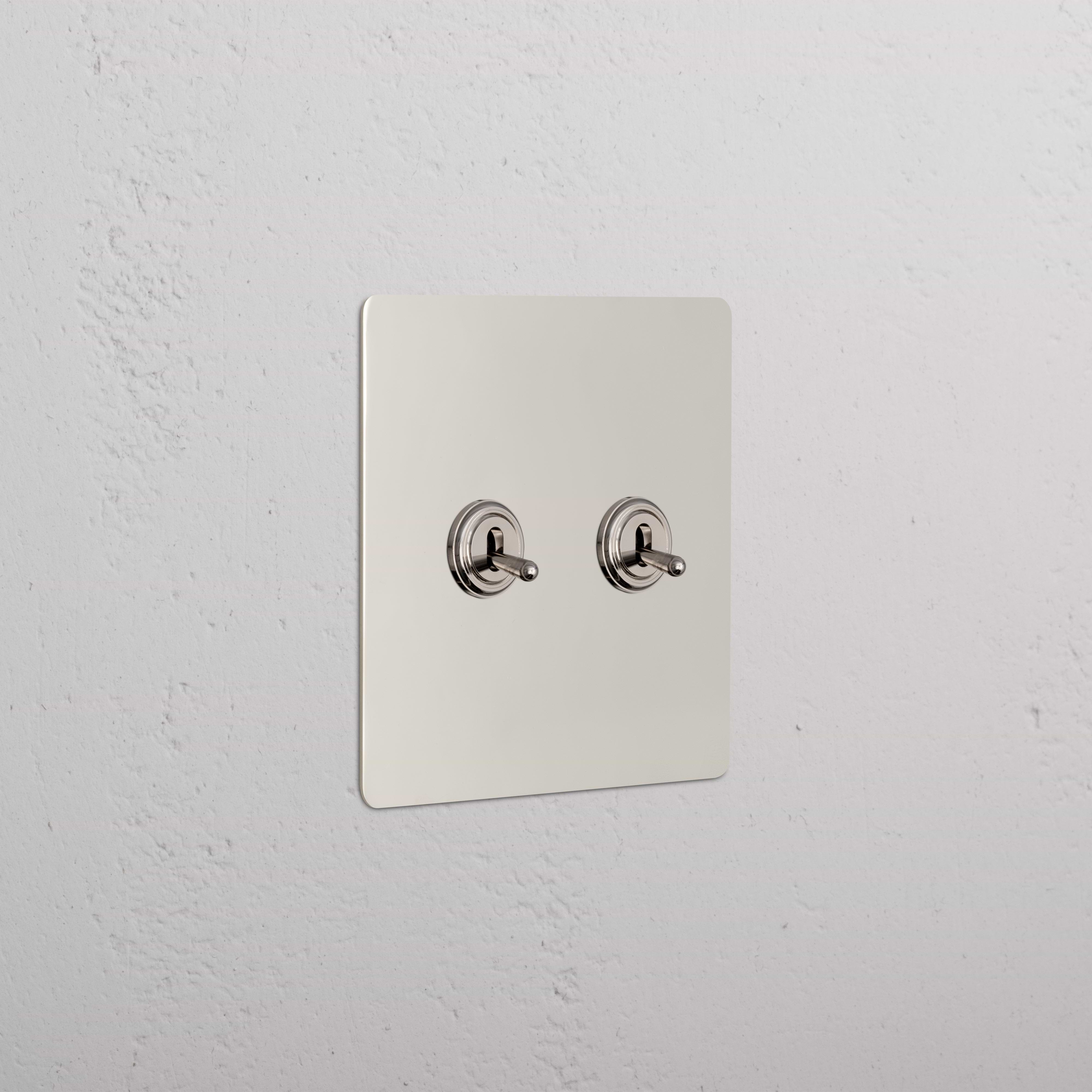 Kew 2G Toggle Switch in polished nickel with two toggle switches on a metallic plate, mounted on a wall.