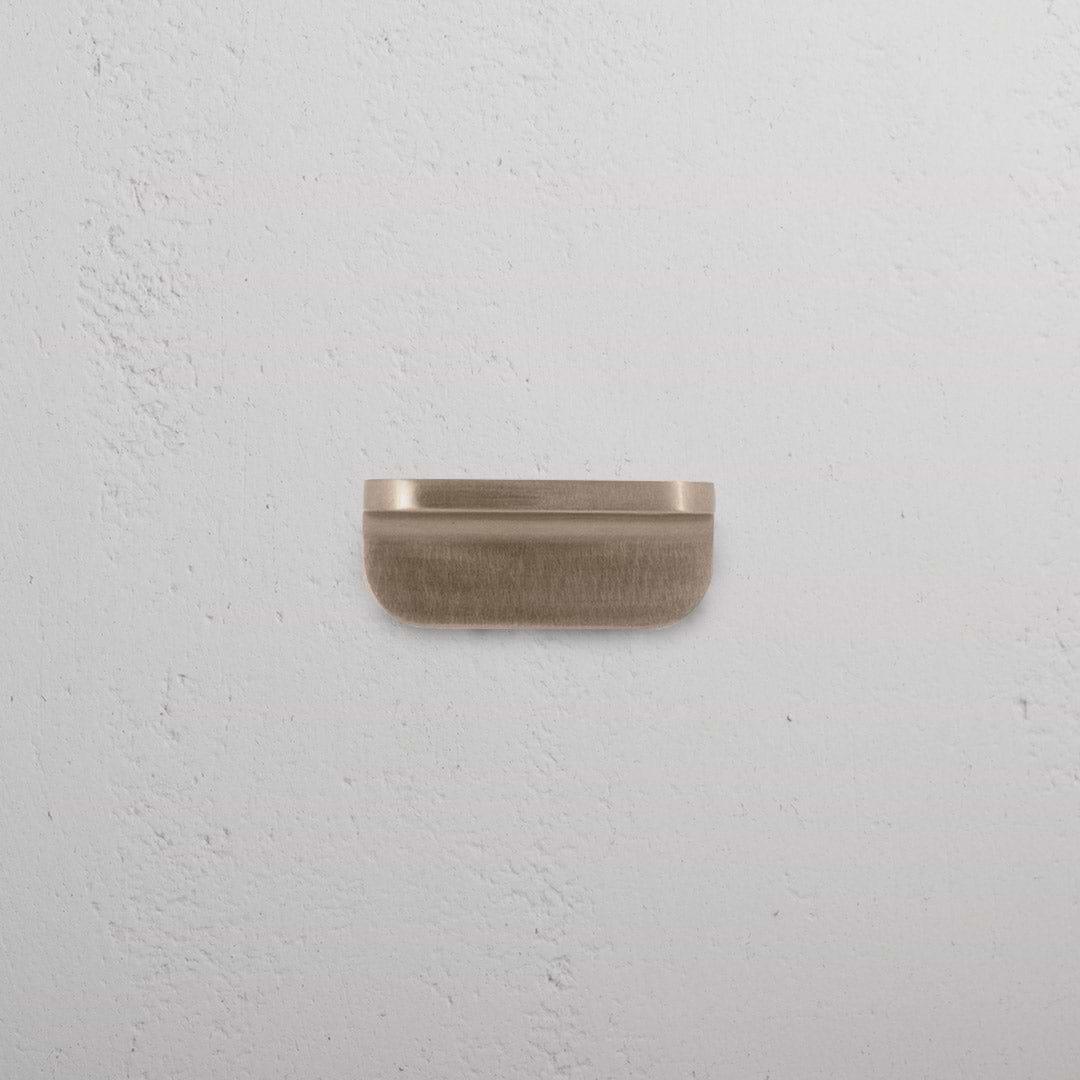 Oxford Furniture Handle Extra Small in Antique Brass, rectangular pull handle on a white textured surface.