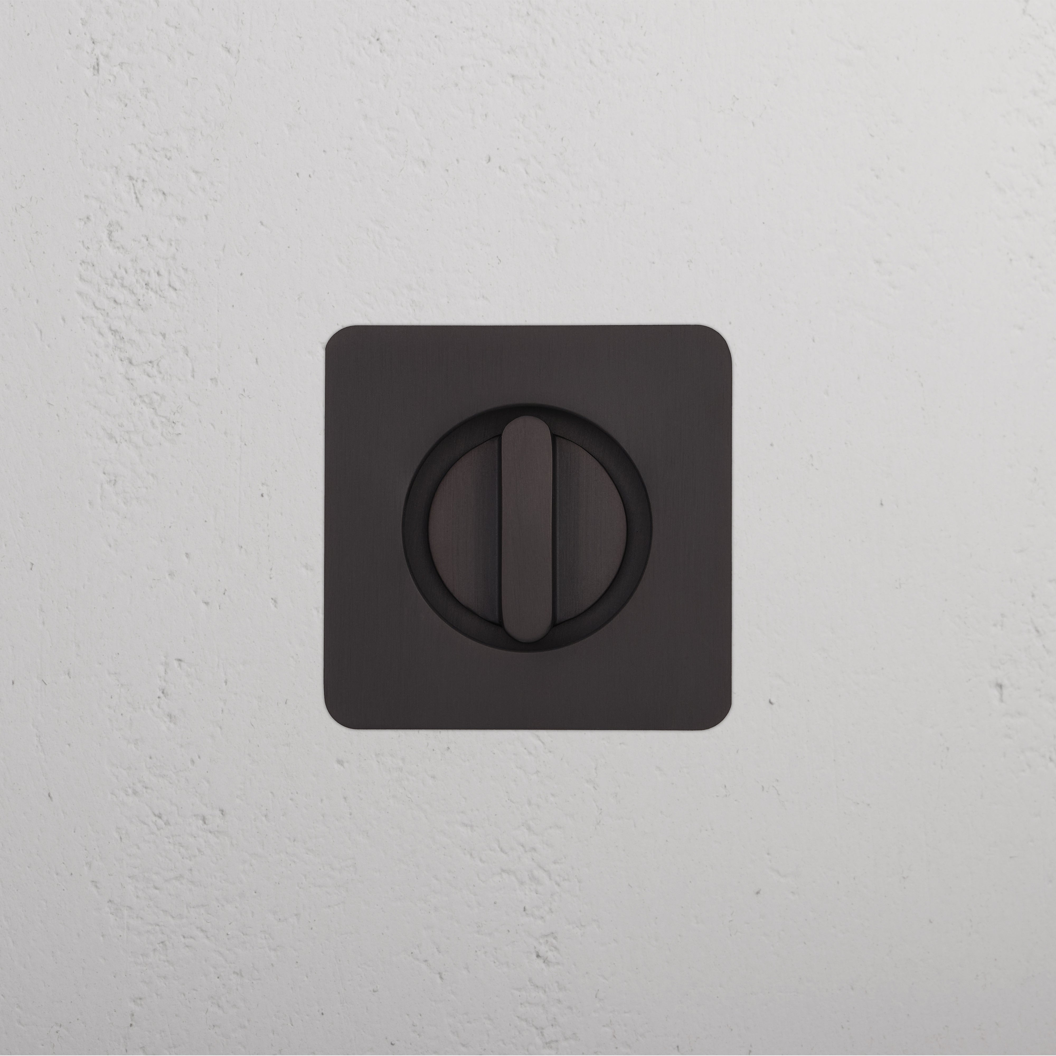 Bronze Regent Recessed Thumbturn with central rotating knob, mounted on a textured white wall.