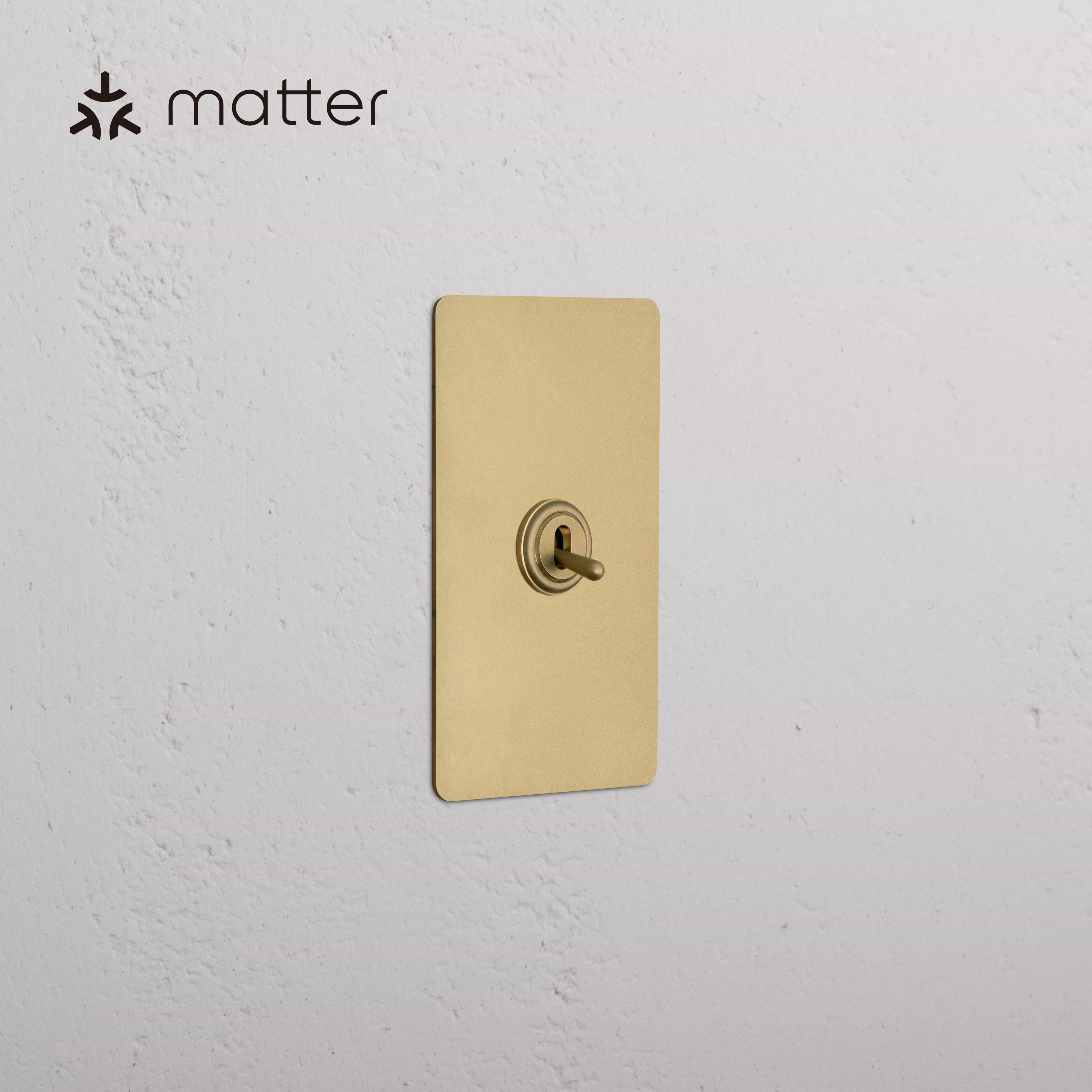 Kew 1G Smart Retractive Toggle Switch in Antique Brass, mounted on a white textured wall.