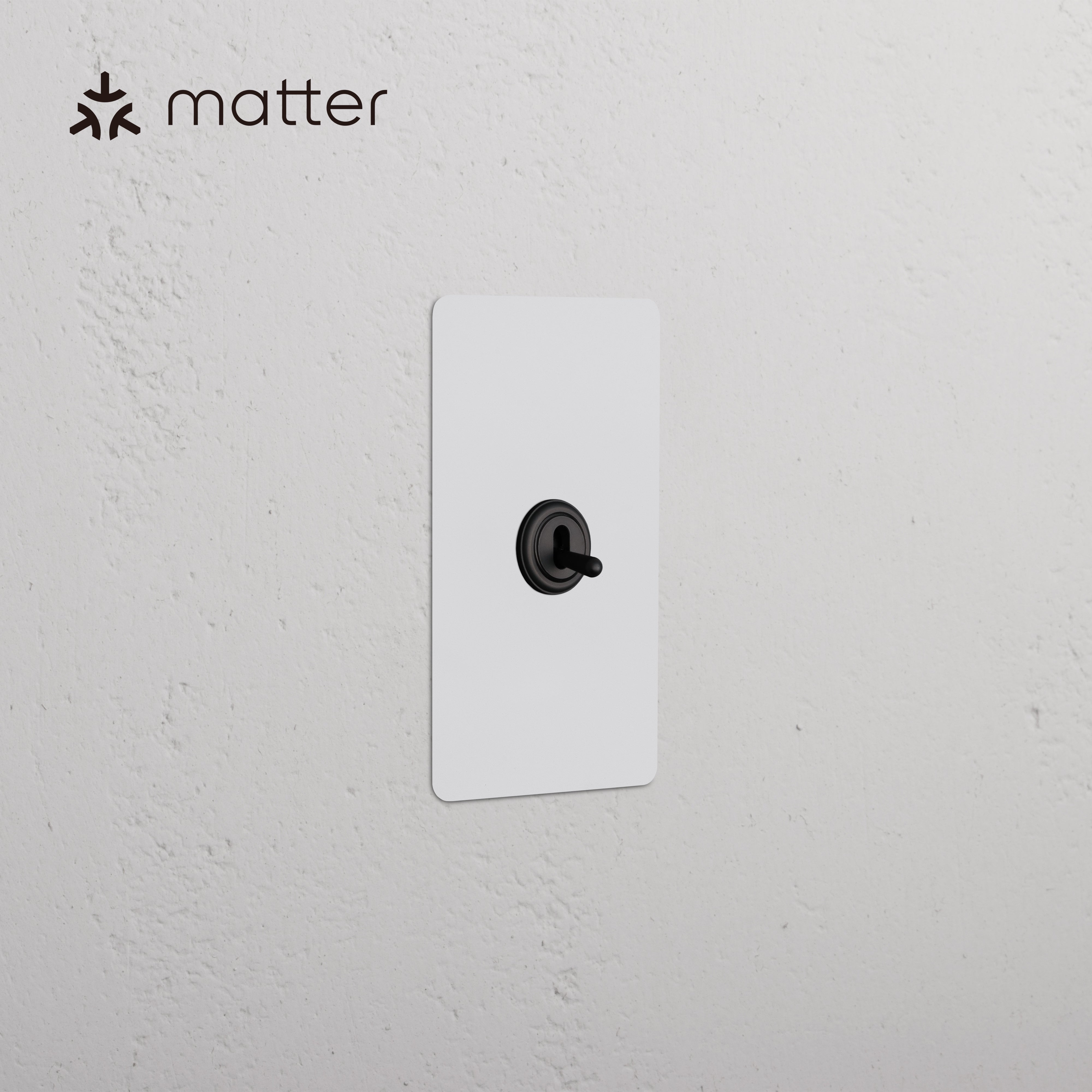 Kew 1G Smart Retractive Toggle Switch in paintable bronze finish with black toggle, shown on white wall.
