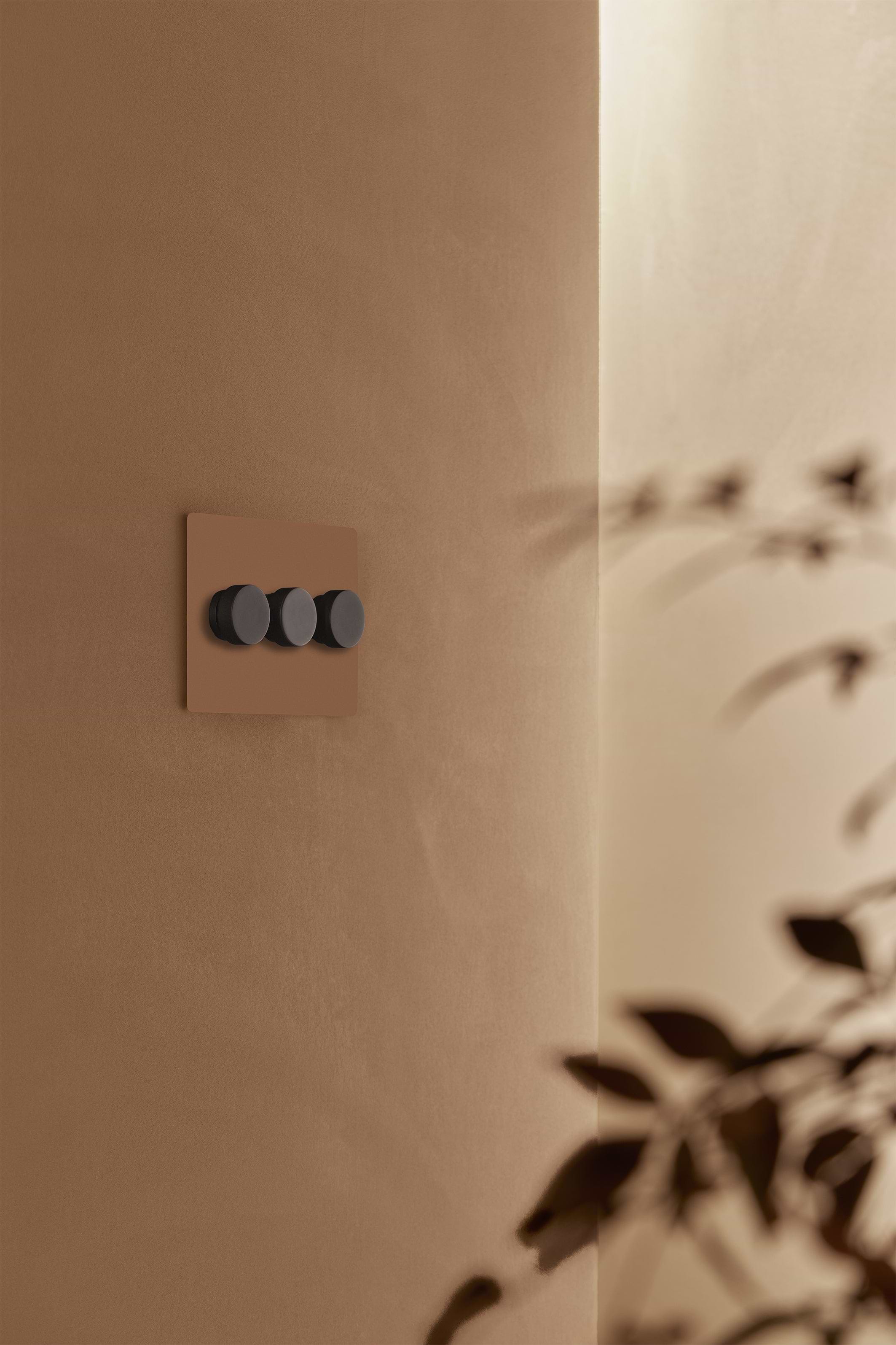 Kew 3G Dimmer Switch in paintable bronze finish with three black knobs, mounted on a beige wall.