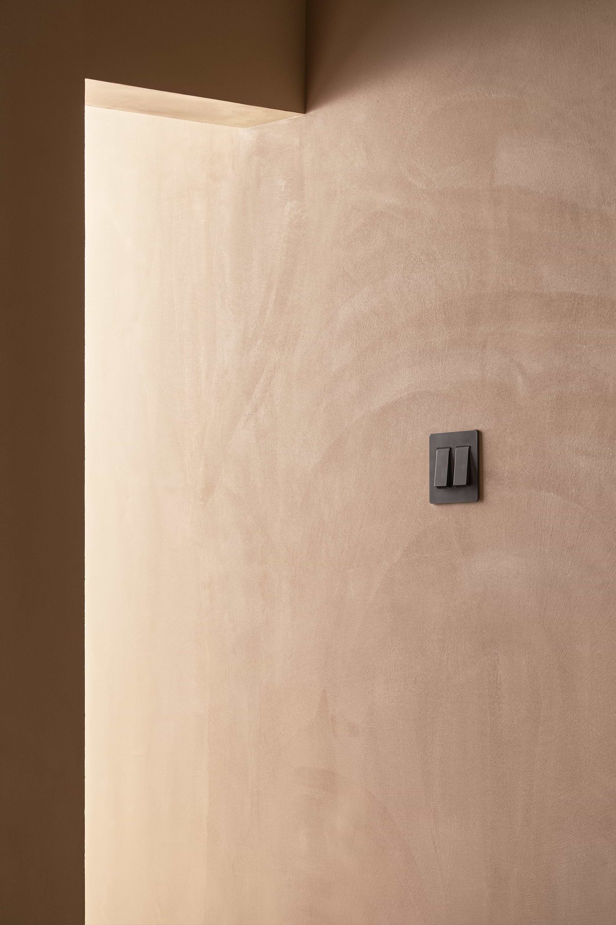 Kew 2G Rocker Switch in Bronze Black mounted on a wall, showing two rocker switch buttons.