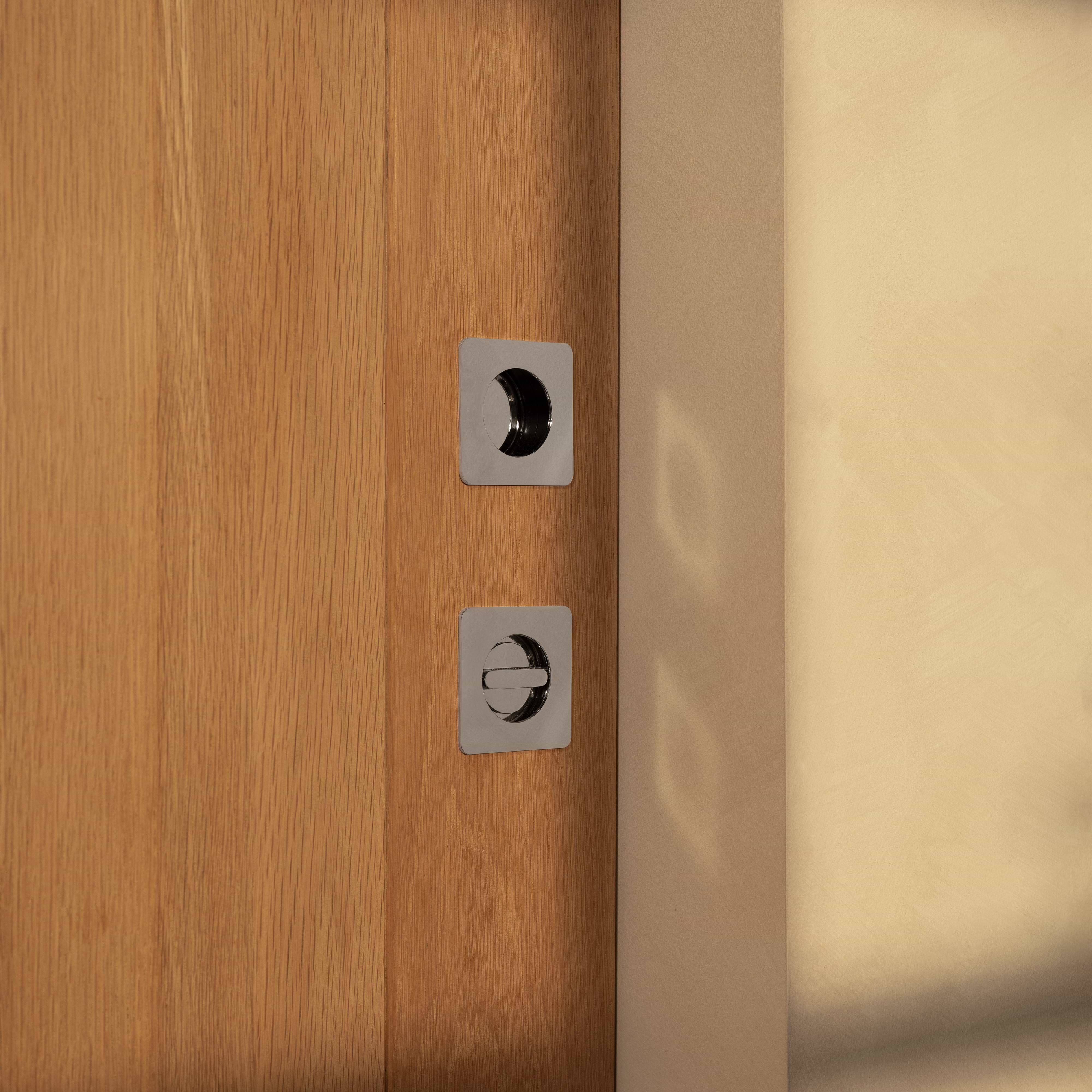 Close-up of a Regent Recessed Small Pull in Polished Nickel installed on a wooden surface.