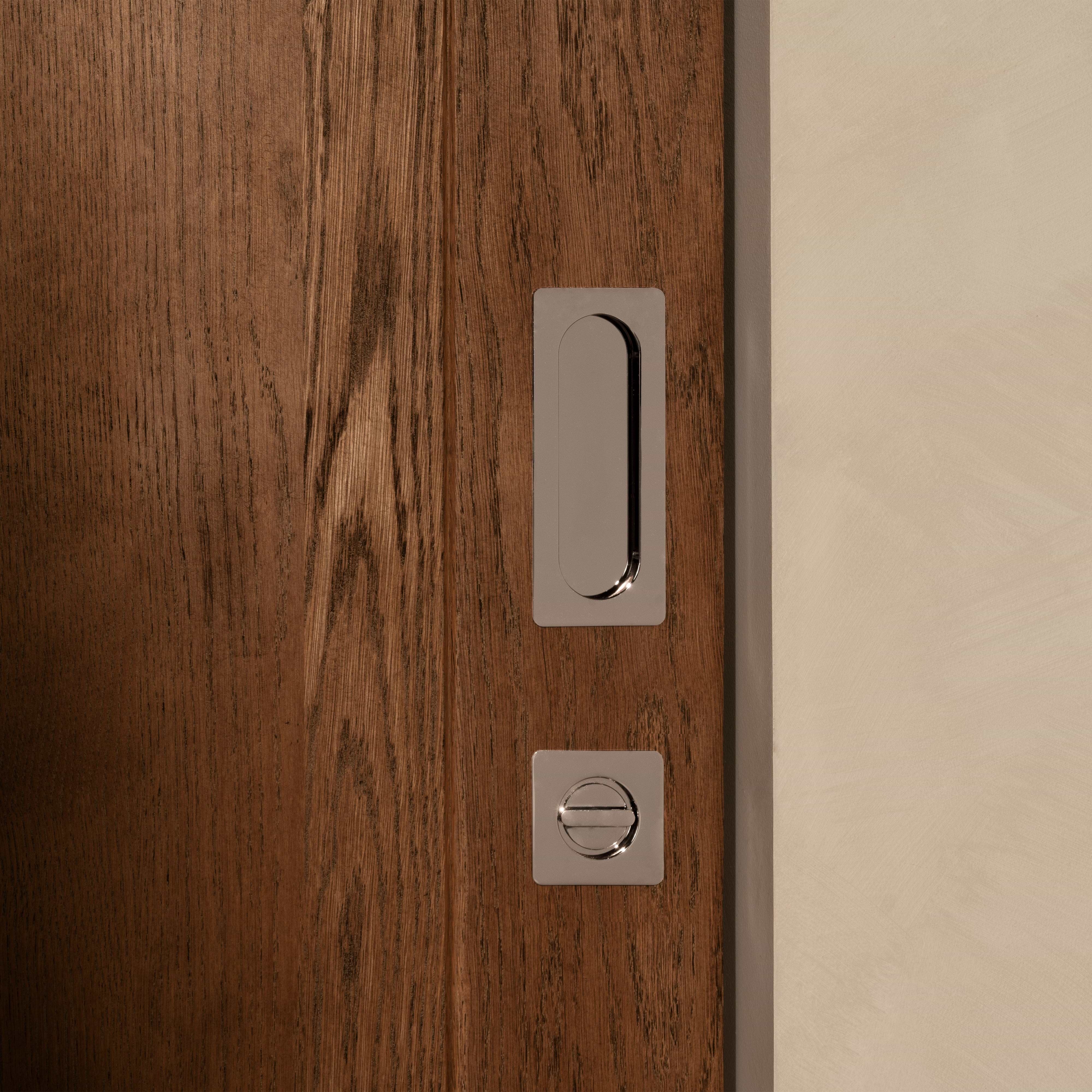 Regent Recessed Medium Pull in polished nickel installed on a wooden sliding door, viewed close-up.