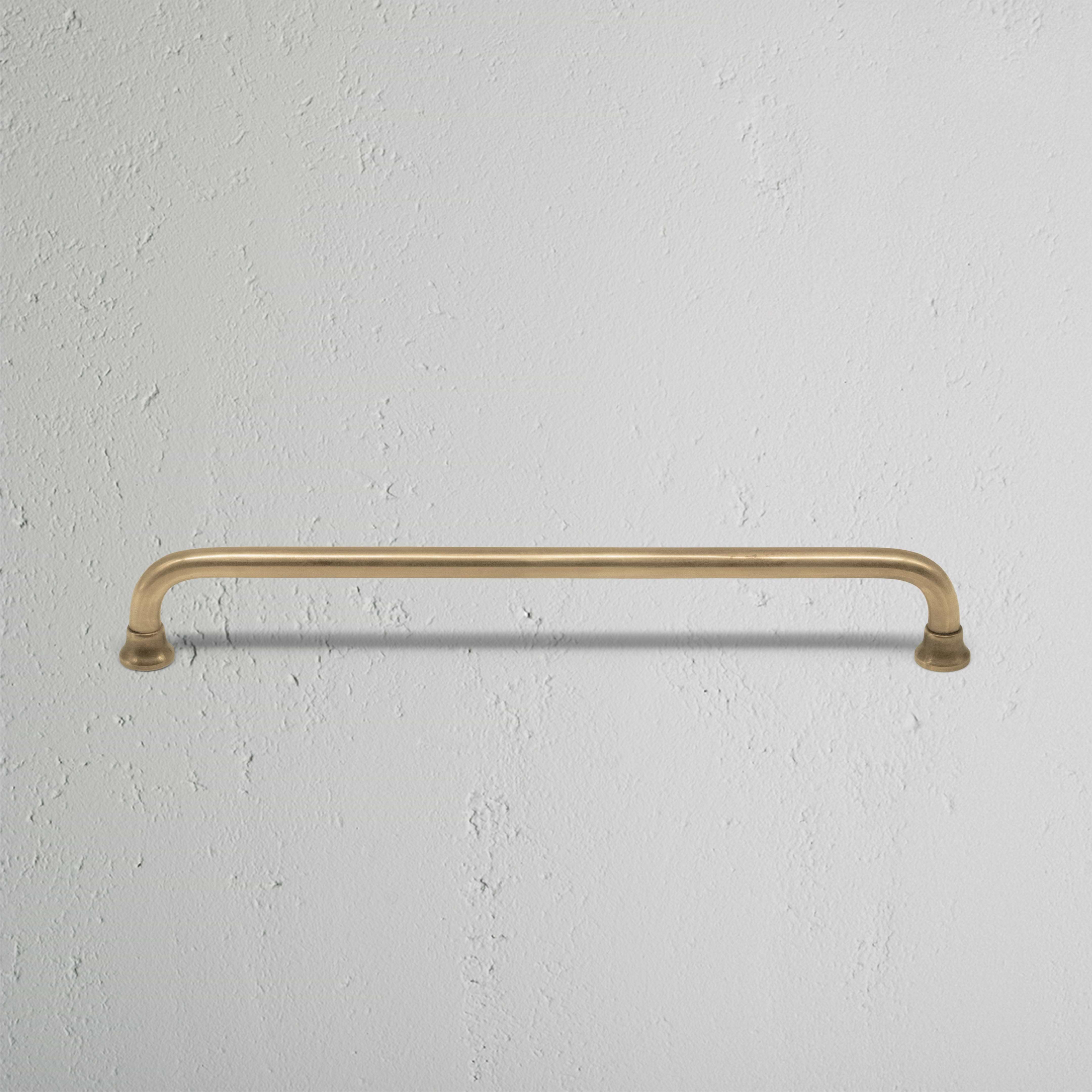 Medium Sycamore Furniture Handle in antique brass finish, shown mounted on a white textured surface.