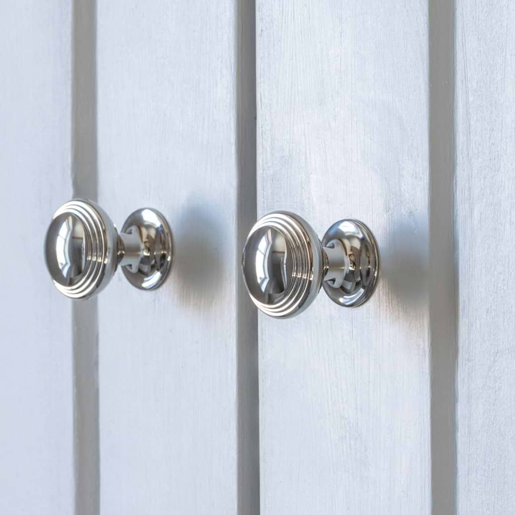 Two small Barlow Furniture Knobs in polished nickel with ridged design on a light gray paneled surface.