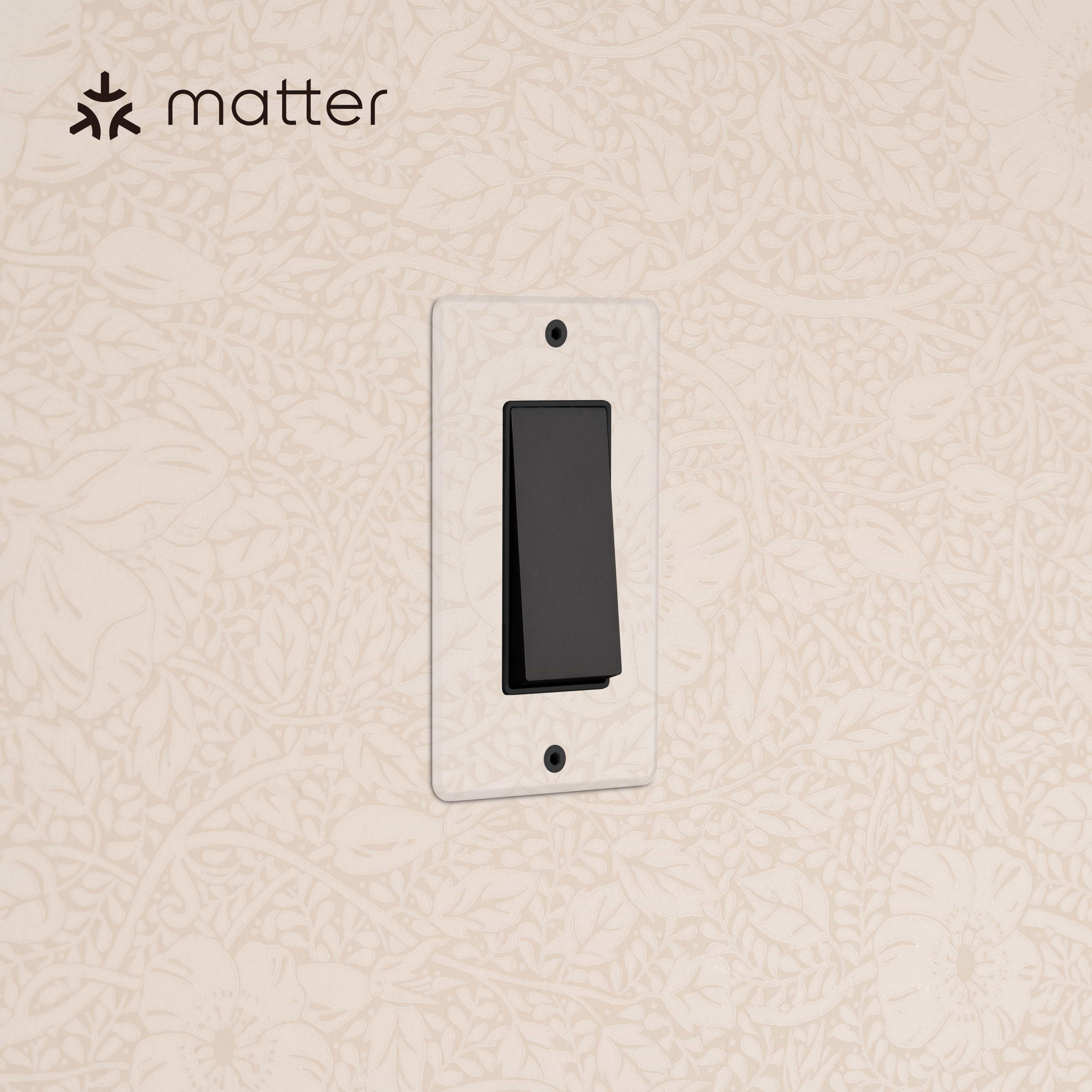 Kew 1G Smart Retractive Rocker Switch in Clear Bronze Black with clear wall plate on a beige patterned wall.