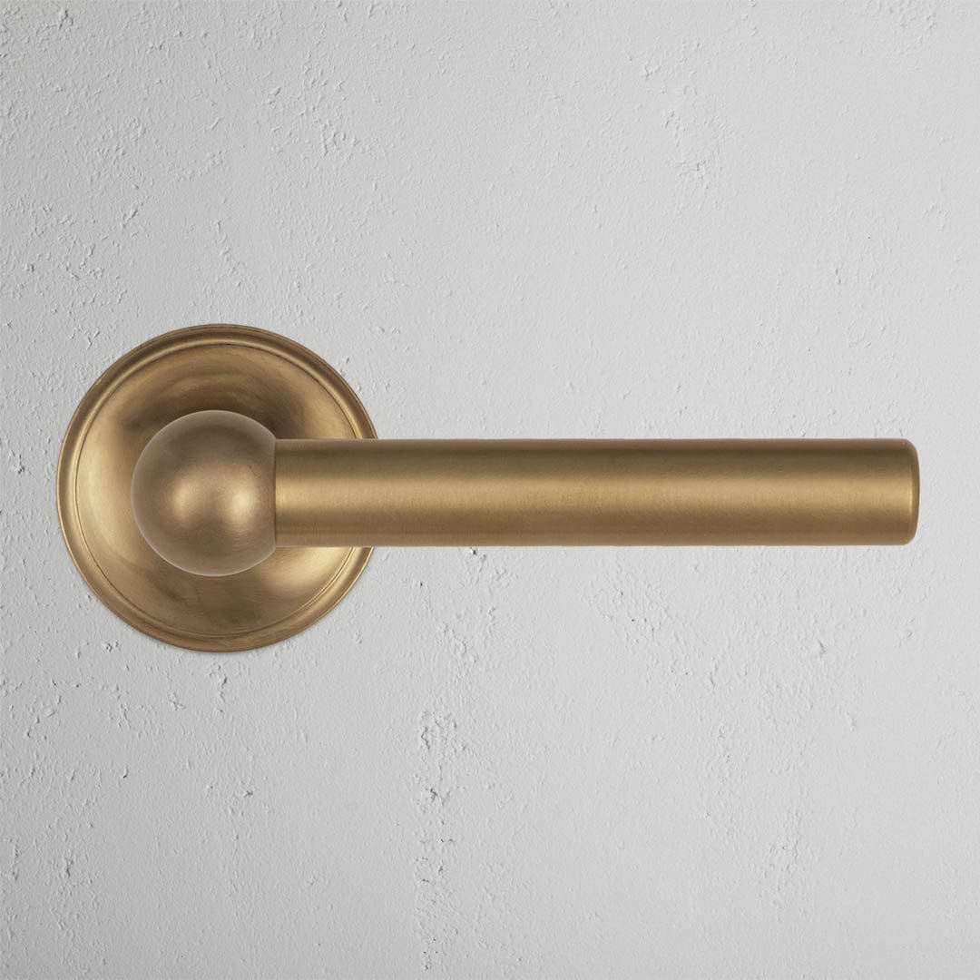 Harper Passage Door Handle Set in antique brass with round backplate, mounted on a white wall.