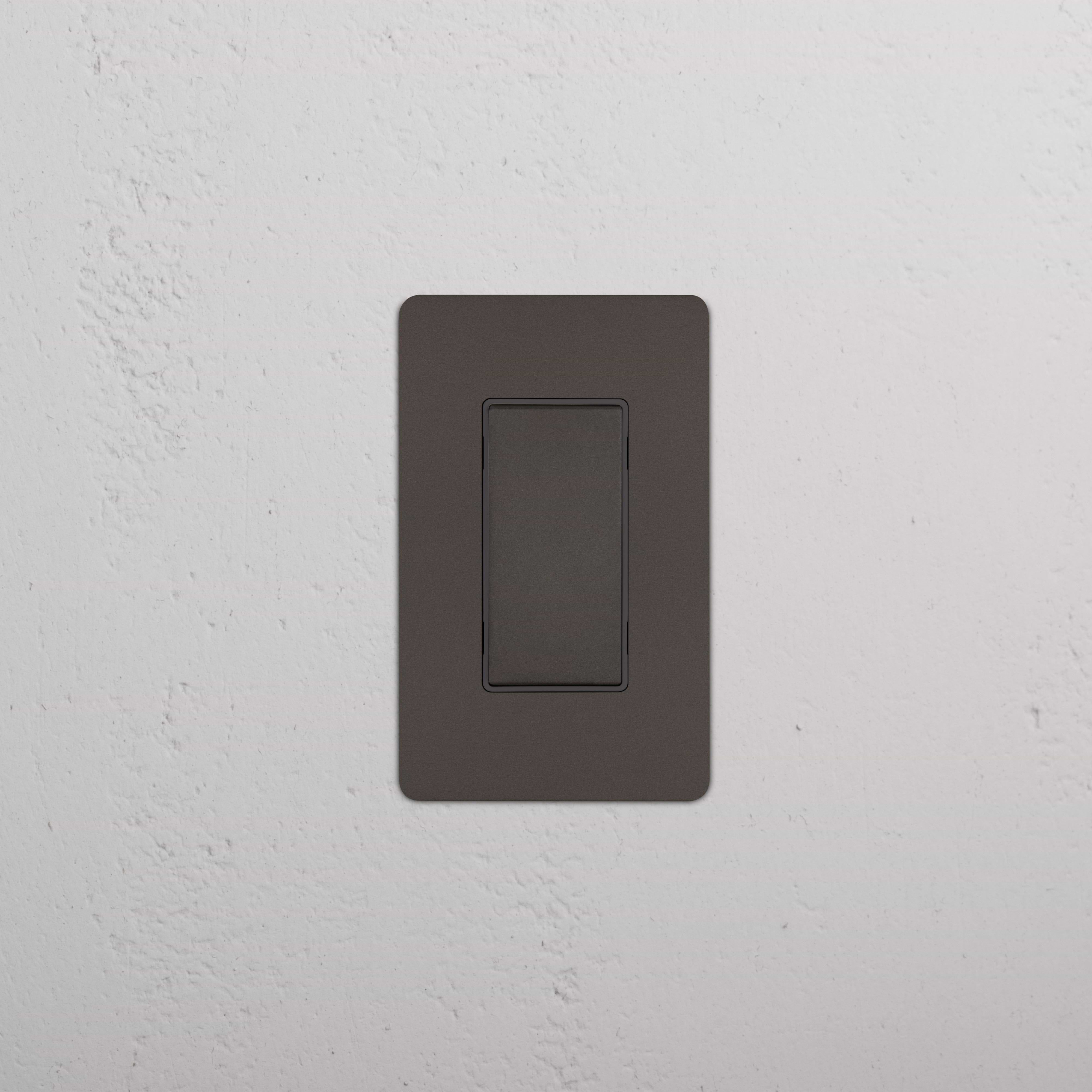 Kew 1G Center Retractive Rocker Switch in Bronze Black with a flat, rectangular design on a white wall.