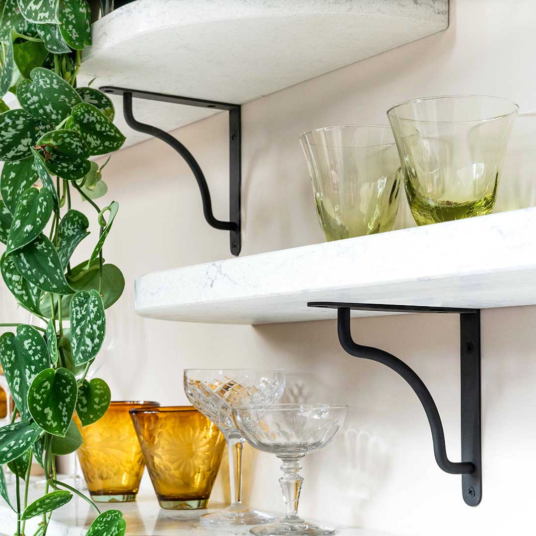 Kilburn Shelf Bracket Small in bronze supporting white shelves with glassware and a trailing plant.