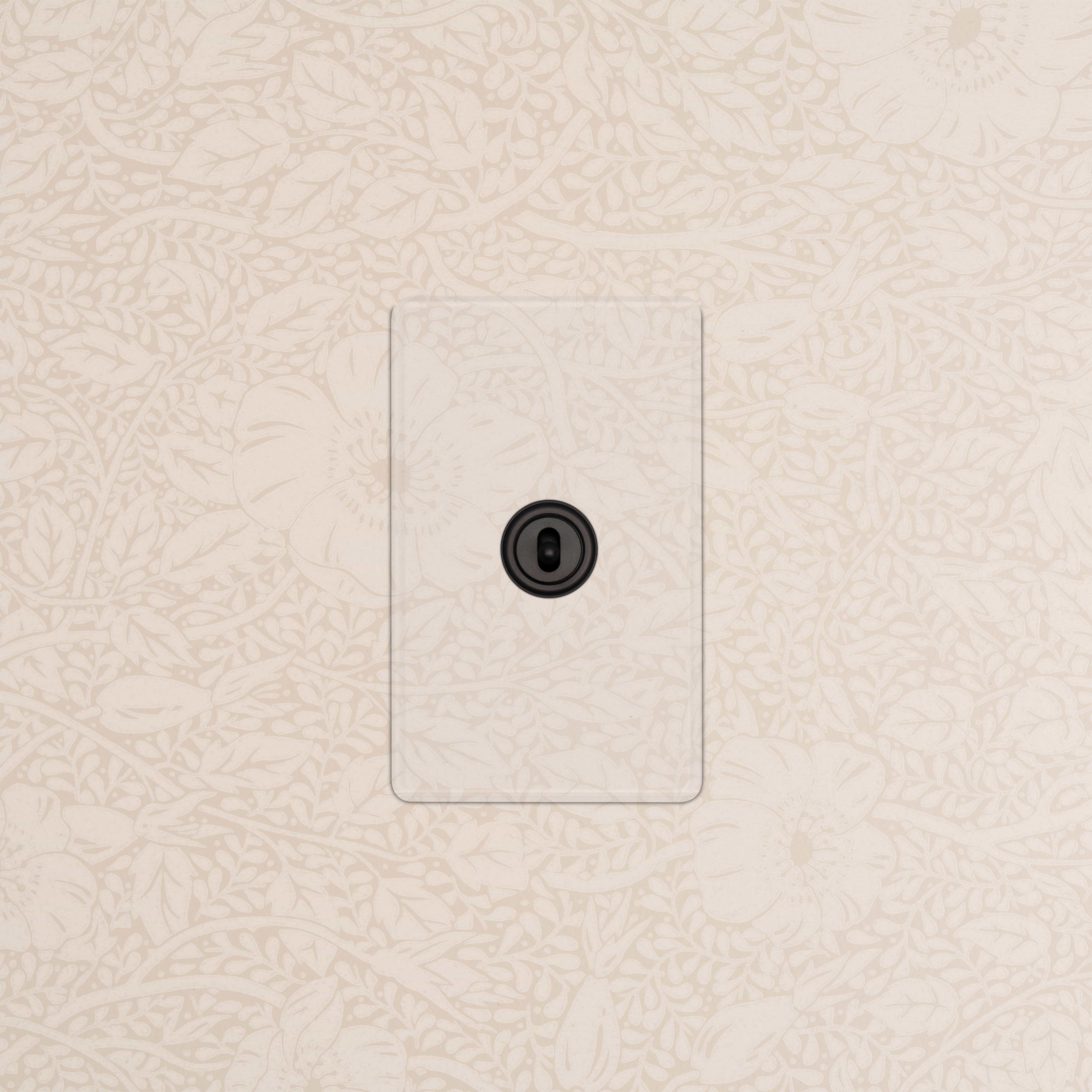 Kew 1G Center Retractive Toggle Switch in Clear Bronze finish, mounted on a patterned beige wall.