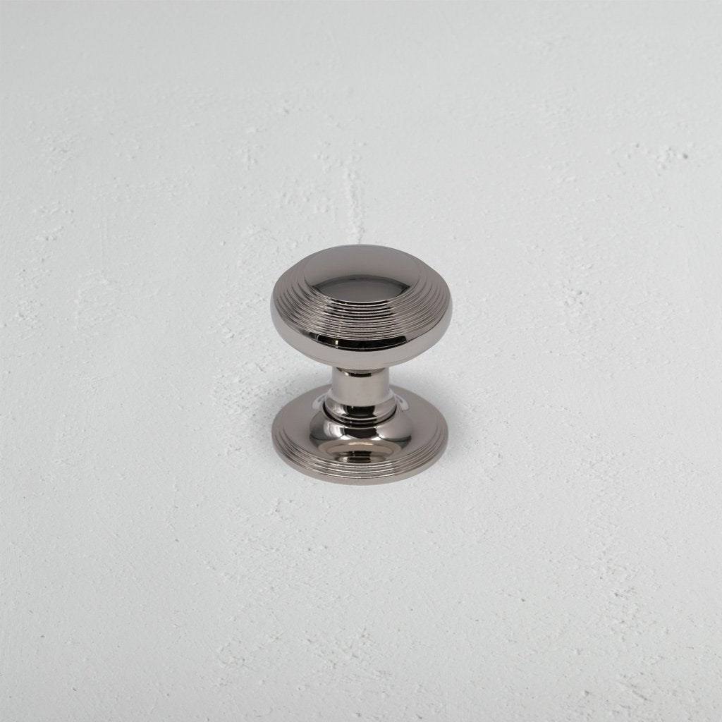 Polished nickel Poplar Dummy Door Knob Set with round shape and subtle grooves on a white surface.