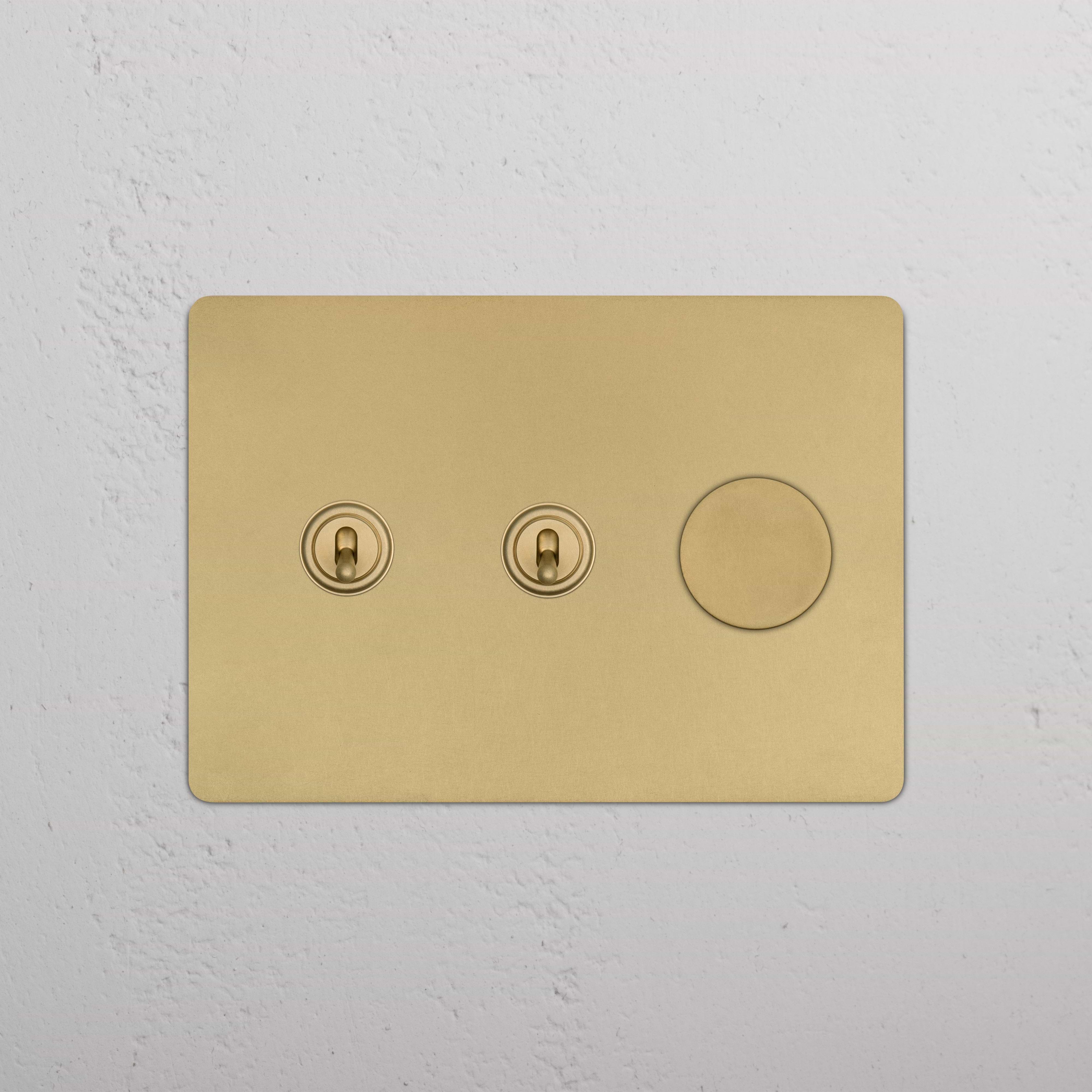 Kew 3G 2x Toggle & Dimmer Switch in antique brass with two toggles and one dimmer, on a white wall.
