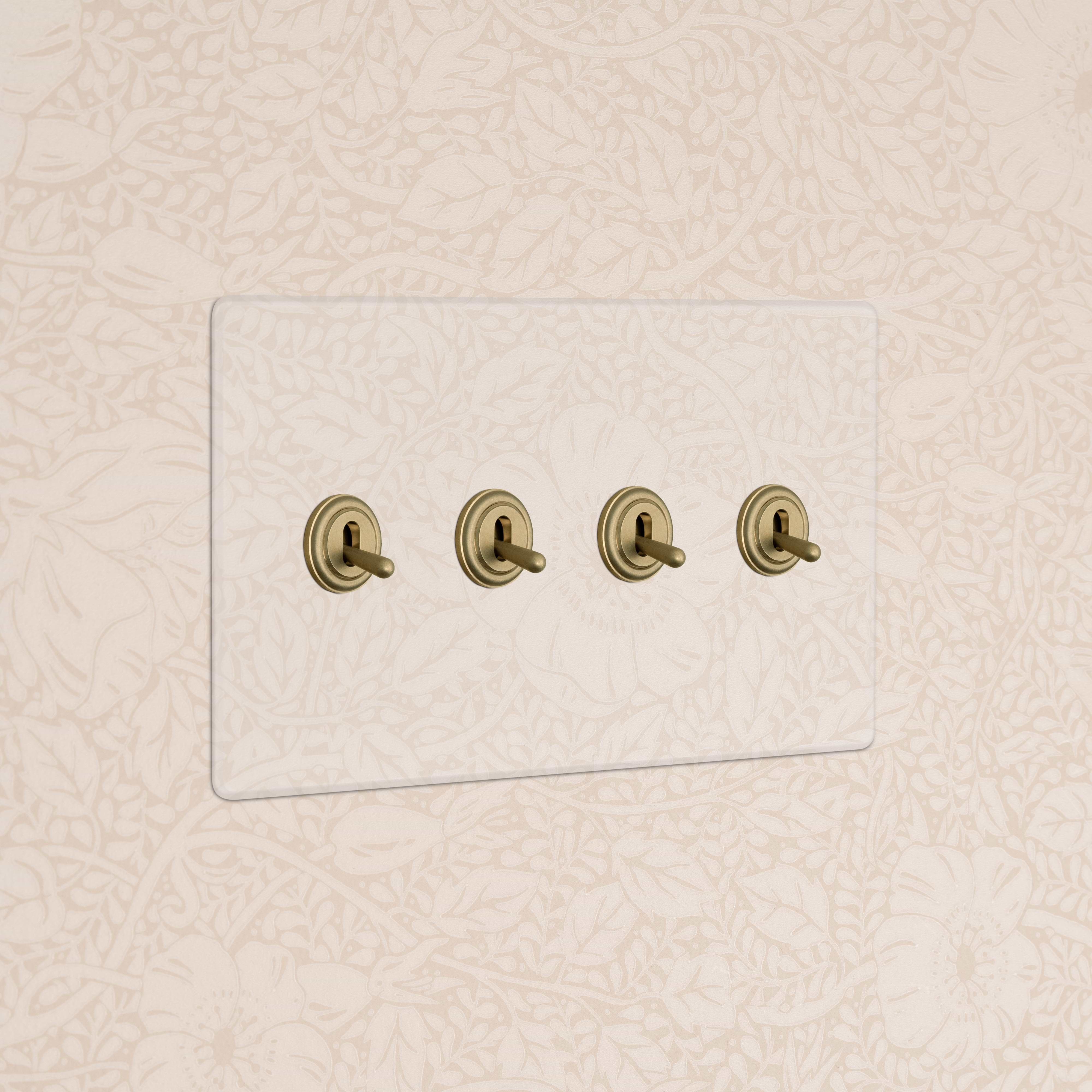 Kew 4G Toggle Switch in Clear Antique Brass with glass plate and four brass toggles on a wall.