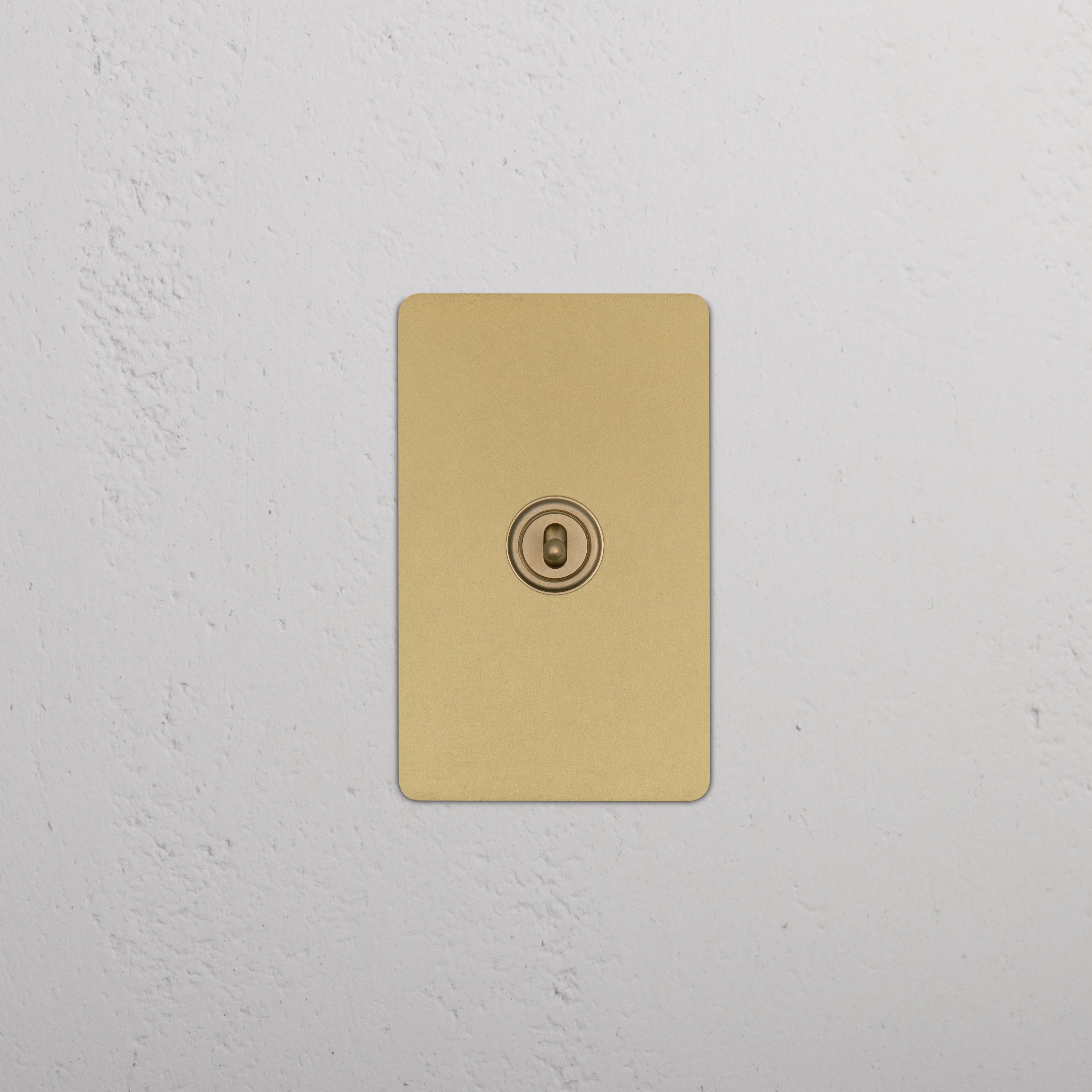 Kew 1G Center Retractive Toggle Switch in antique brass, shown mounted on a white textured wall.