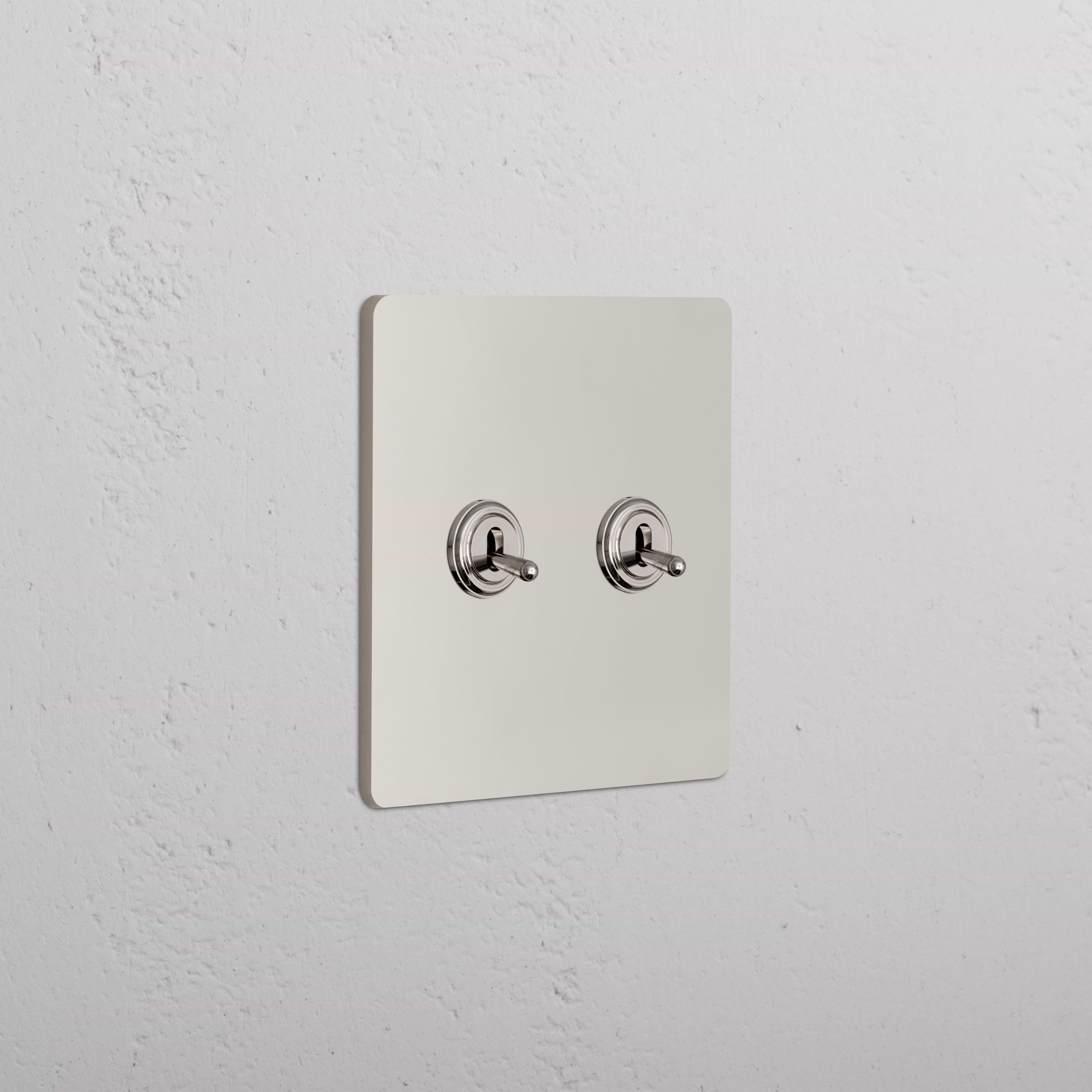 Grove 2G Toggle Switch in polished nickel with two side-by-side toggles, mounted on a white wall.