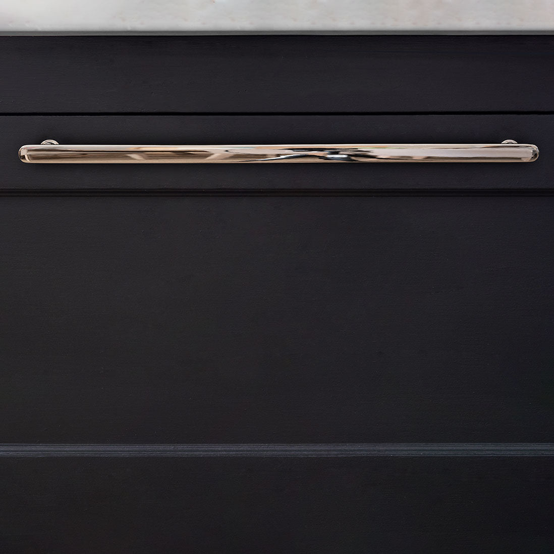Large polished nickel Milliner Furniture Handle mounted on a cabinet beneath a white countertop.