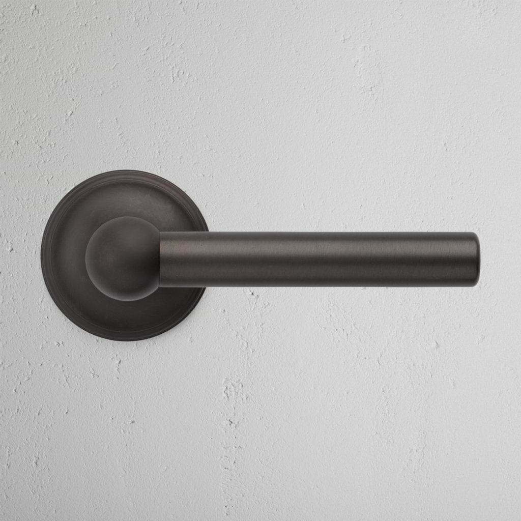 Harper Dummy Door Handle Set in bronze finish with a round base, mounted on a white textured wall.