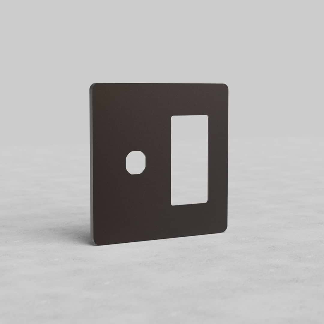 Bronze 2-gang switch and outlet plate (Grove US) with one round and one rectangular cutout, upright on a light surface.
