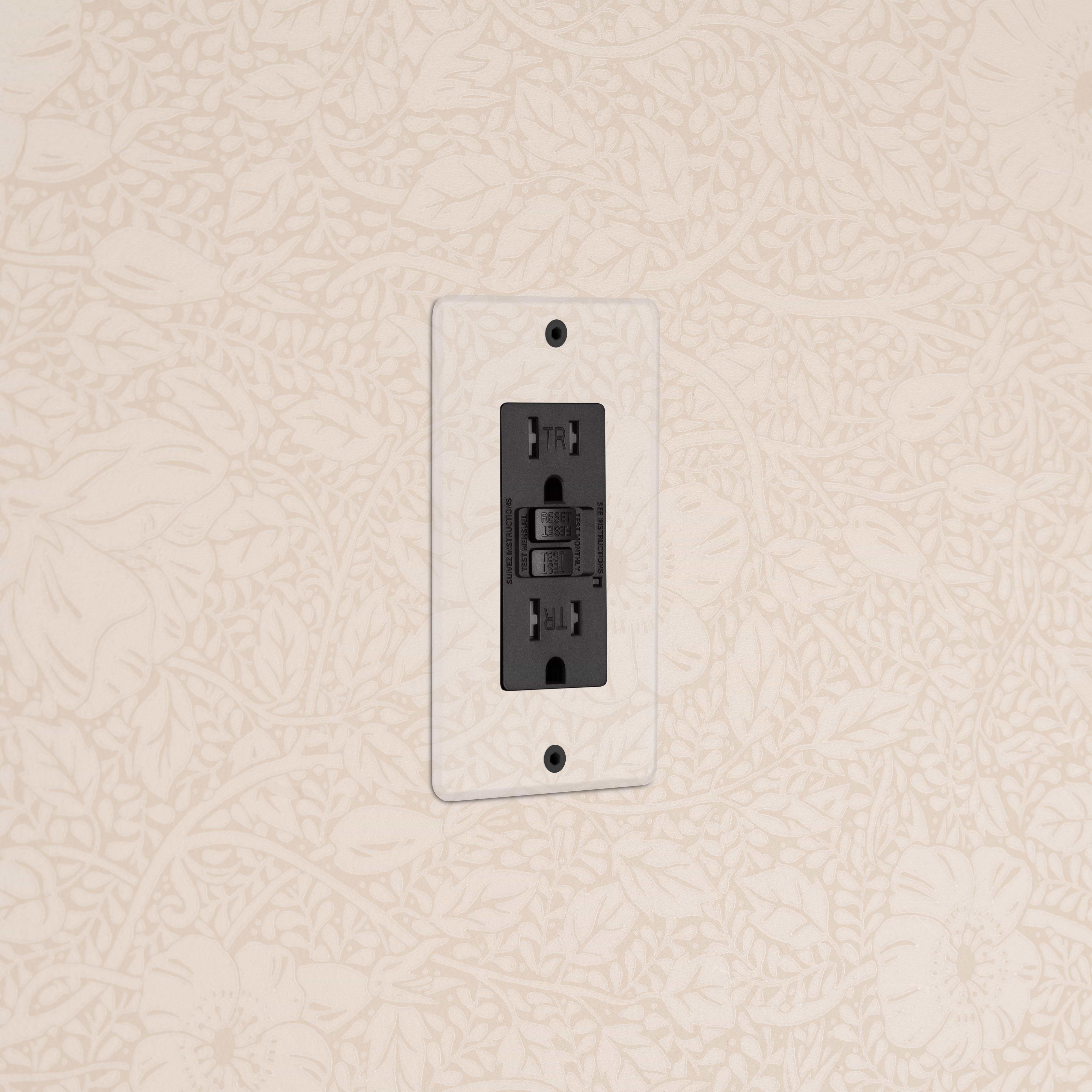 Kew 1G 15A GFCI Outlet in Clear Black with reset and test buttons, mounted on a light floral wall.