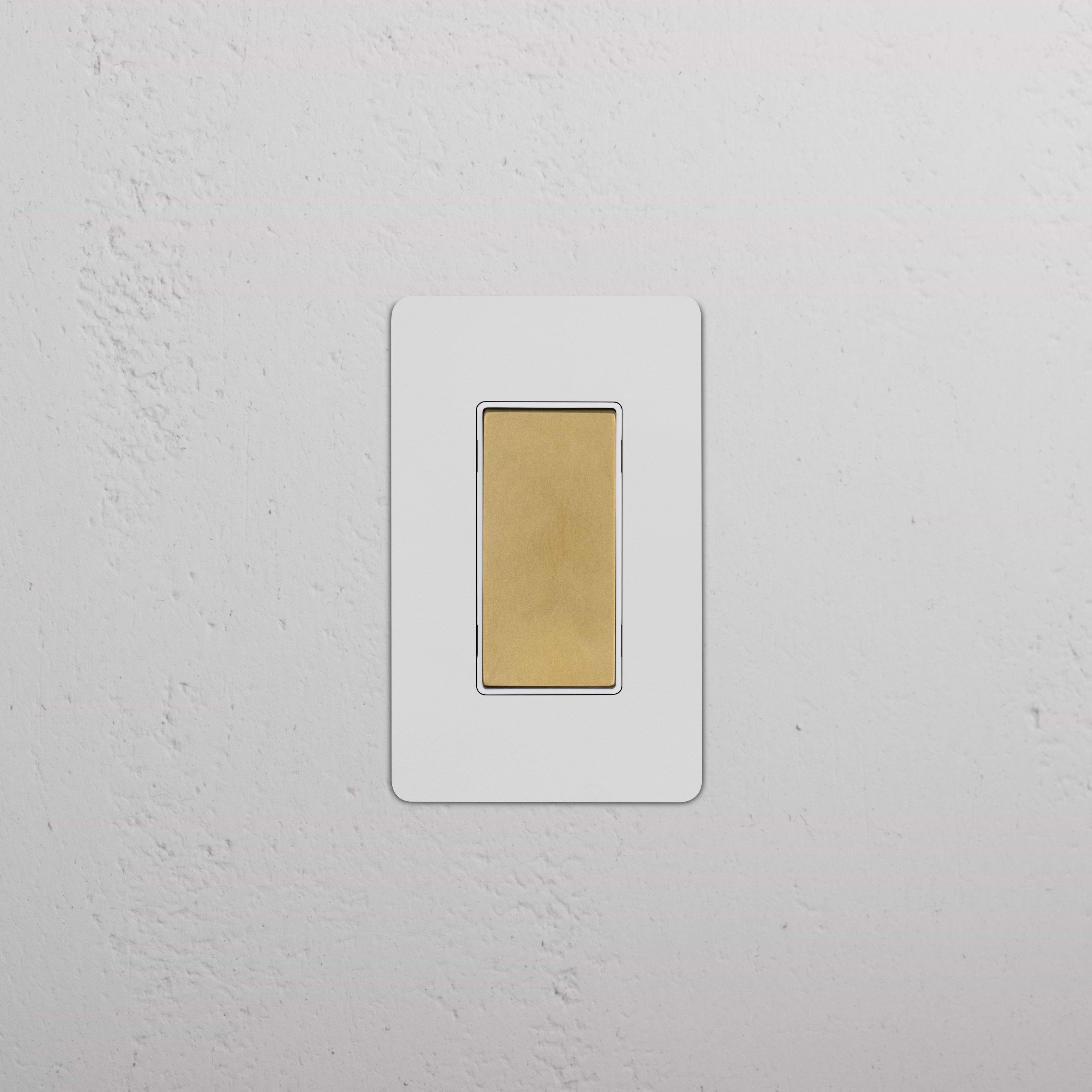 Kew 1G Center Retractive Rocker Switch in paintable antique brass white, shown installed on a white wall.