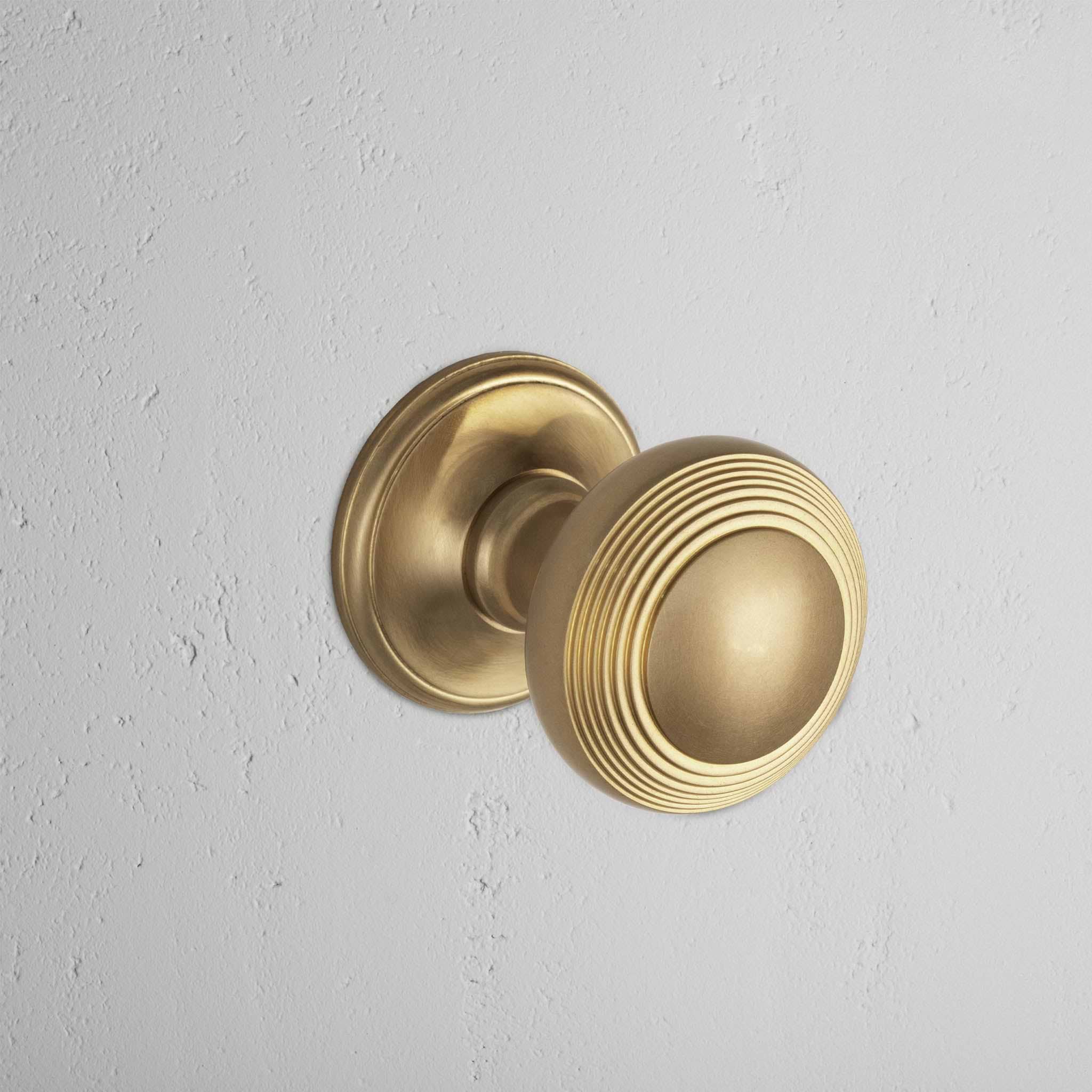 Antique Brass Poplar Unsprung Passage Door Knob Set with ridged circular design mounted on white wall.