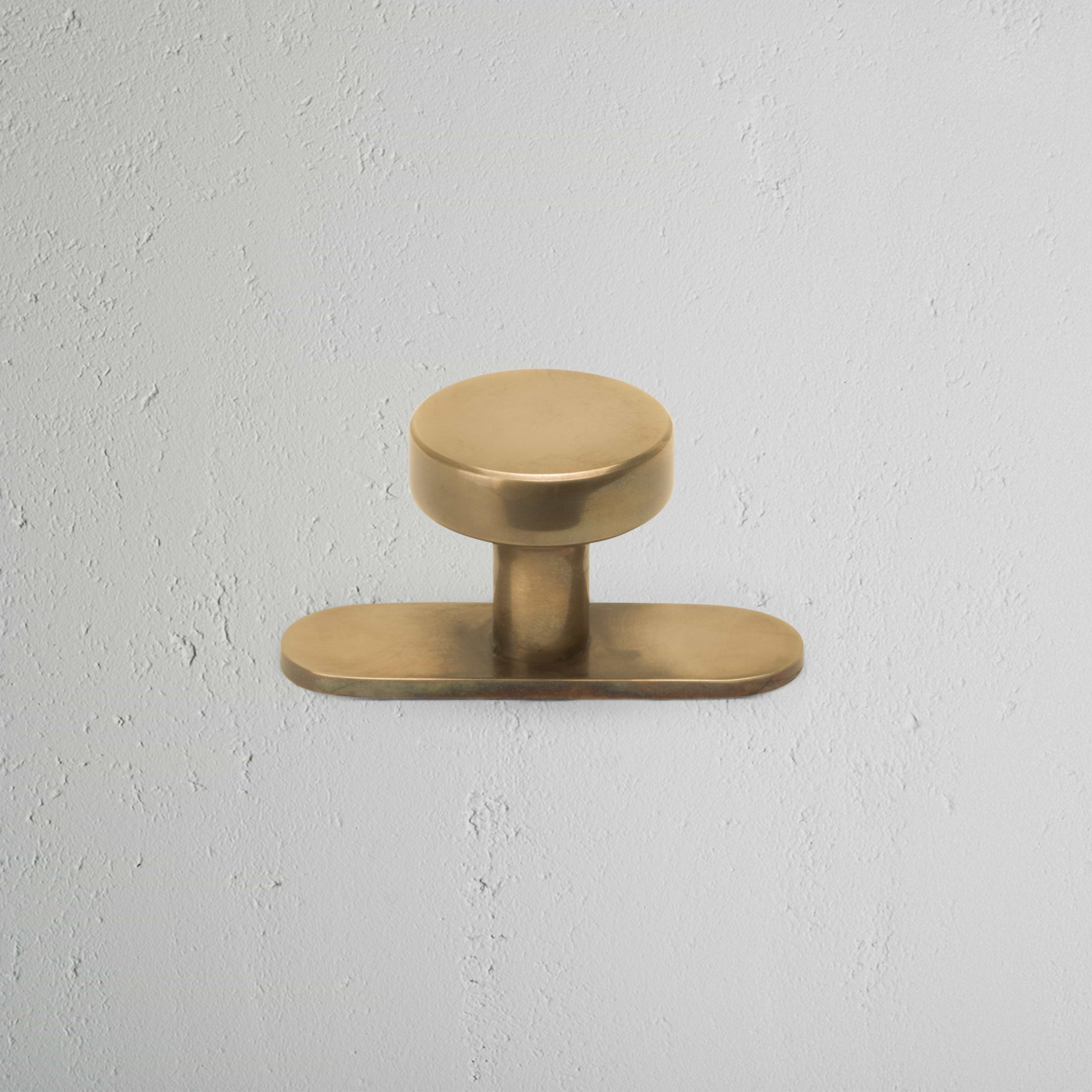 Polished Kilburn Furniture Knob with a round design, mounted on a light textured white wall.
