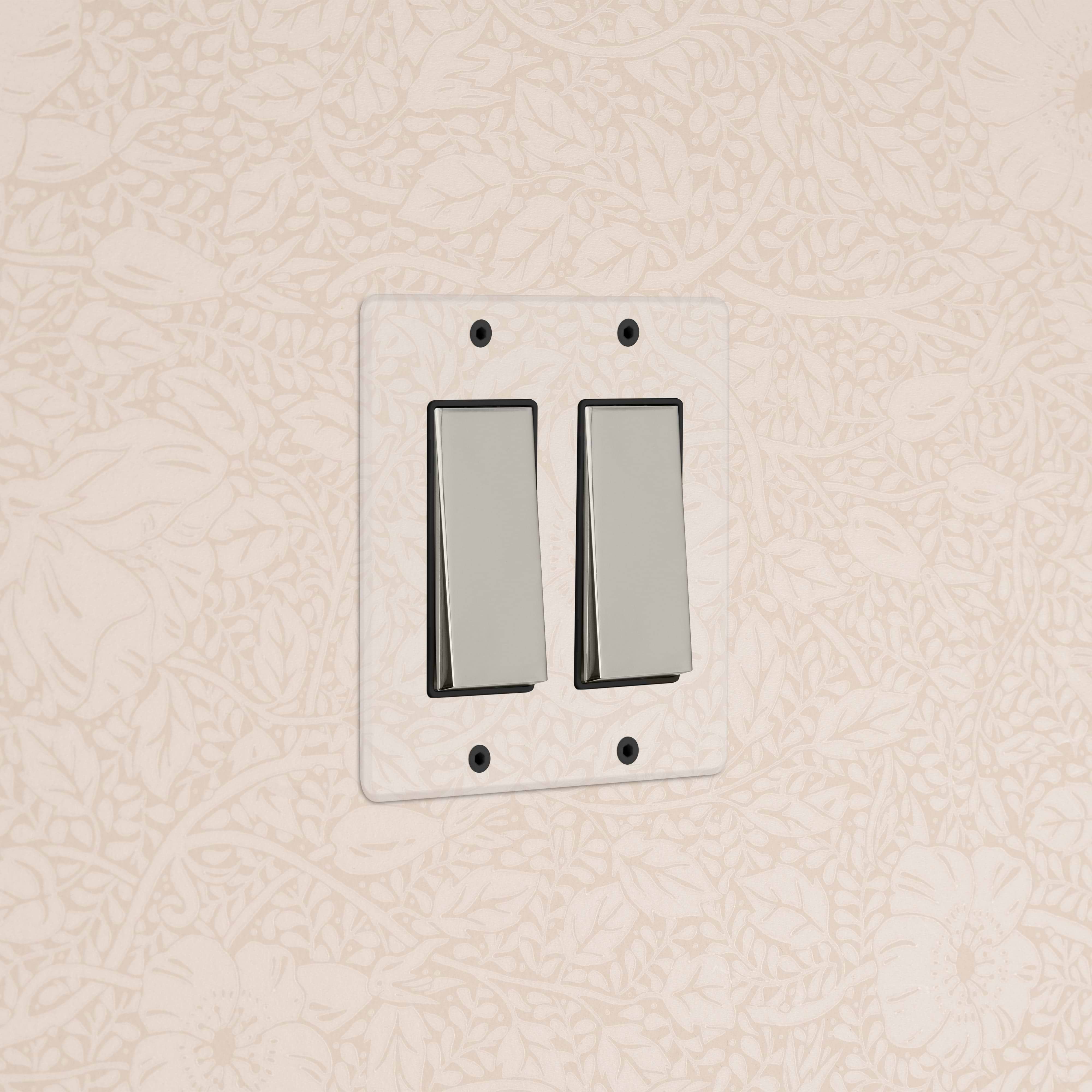 Kew 2G Rocker Switch in clear polished nickel black, double switch, mounted on beige floral wallpaper.