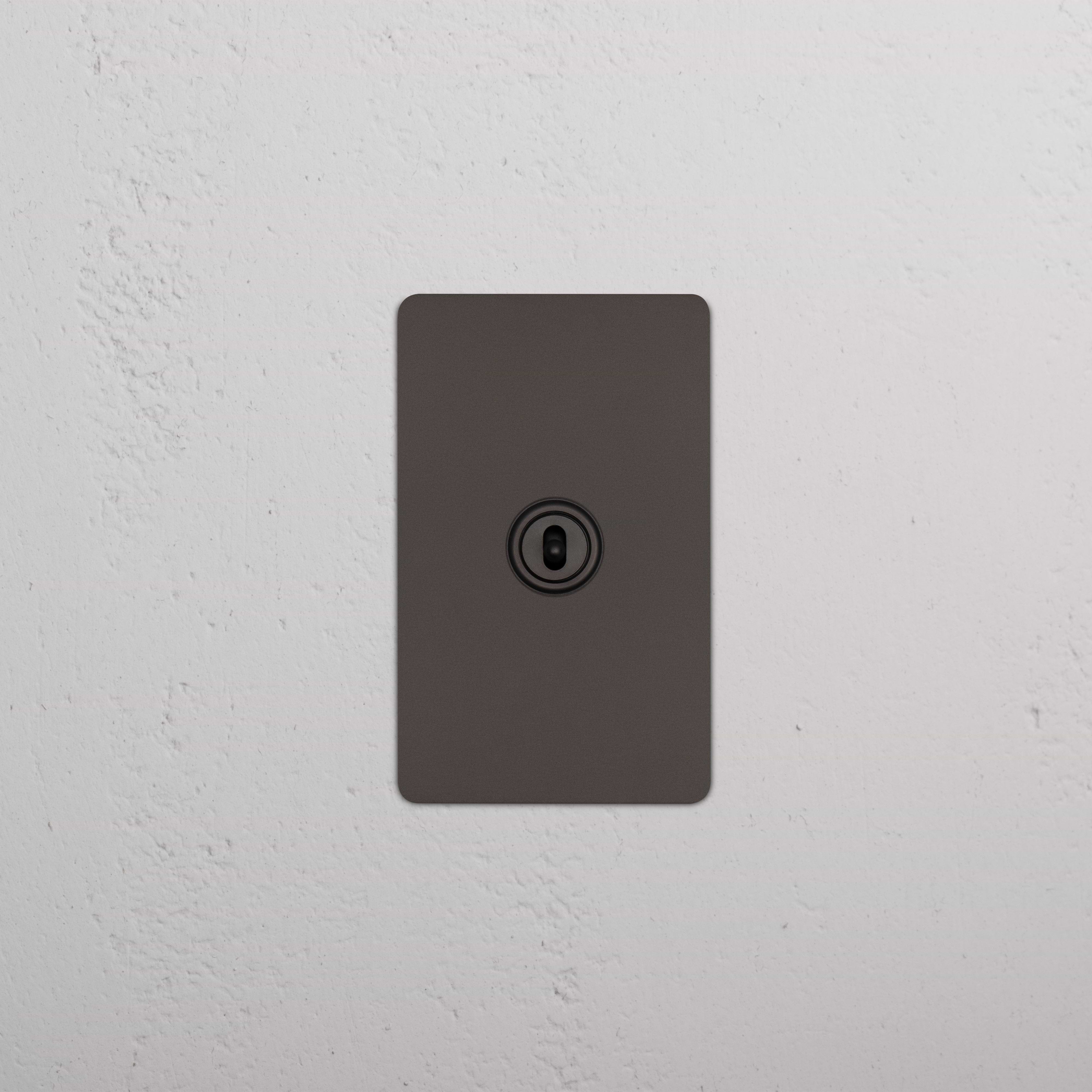 Bronze Kew 1G Center Retractive Toggle Switch featuring a central toggle, installed on a white wall.