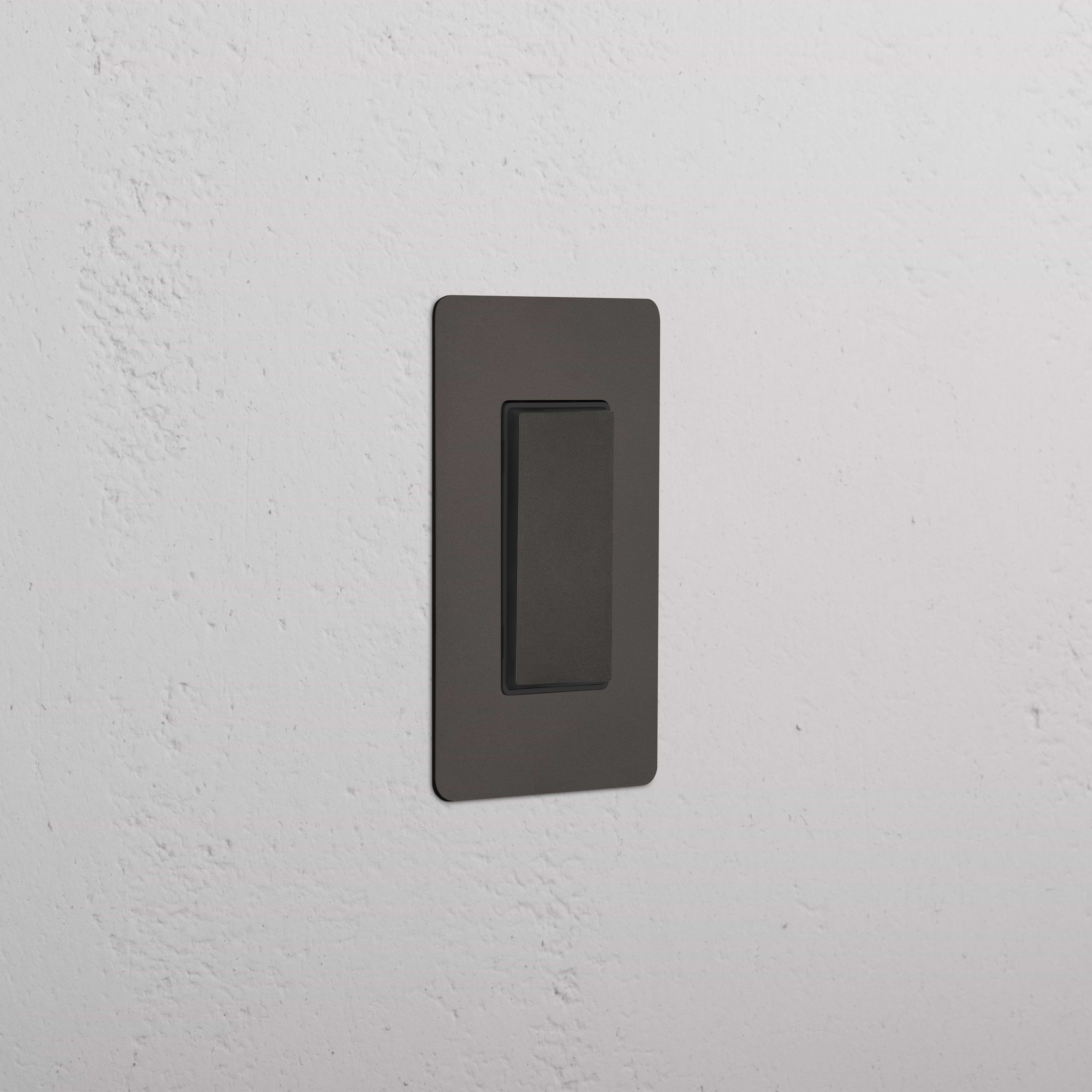 Kew 1G Center Retractive Rocker Switch in Bronze Black installed on a textured white wall.