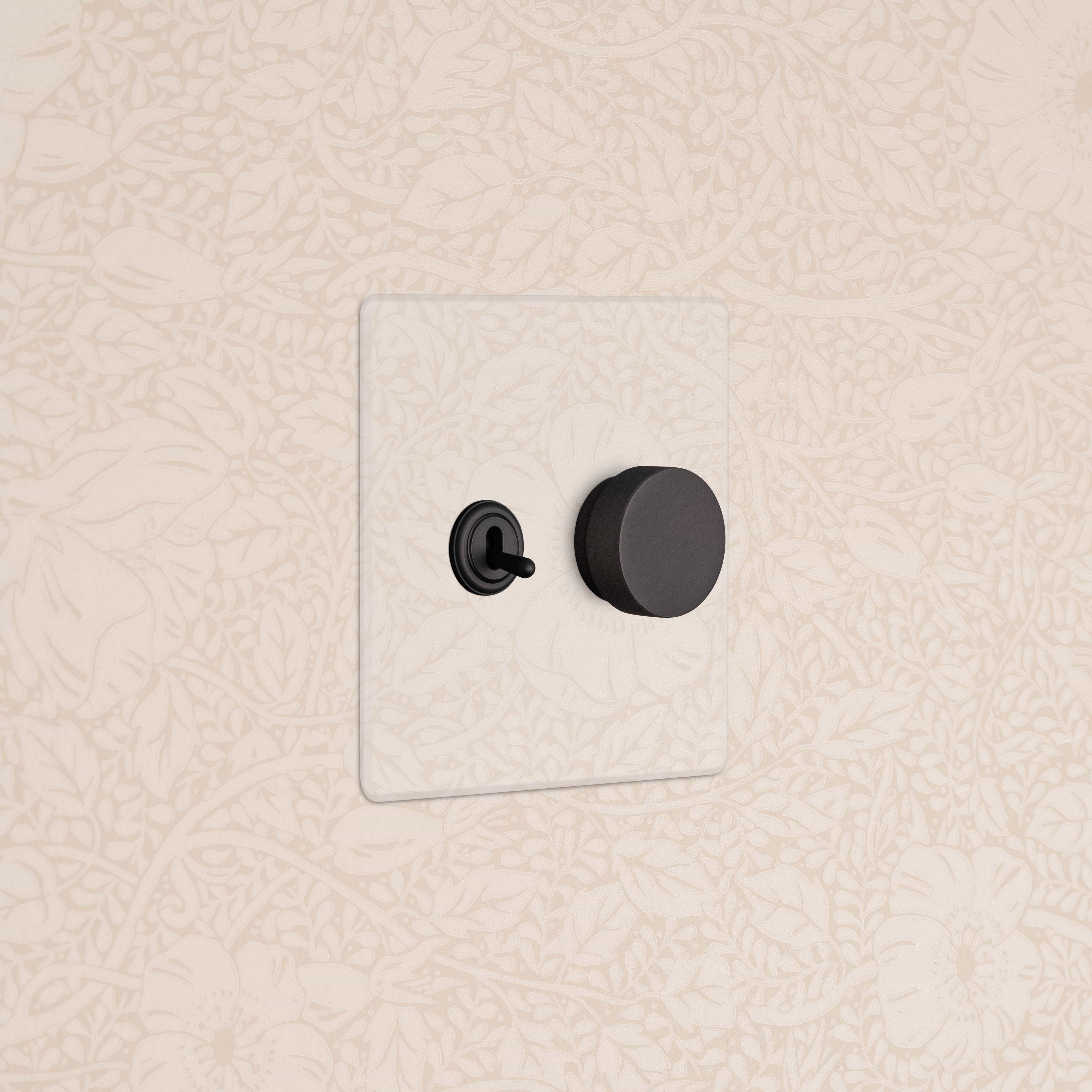 Kew 2G Toggle & Dimmer Switch in clear bronze with black toggle and round dimmer on a beige floral wall.