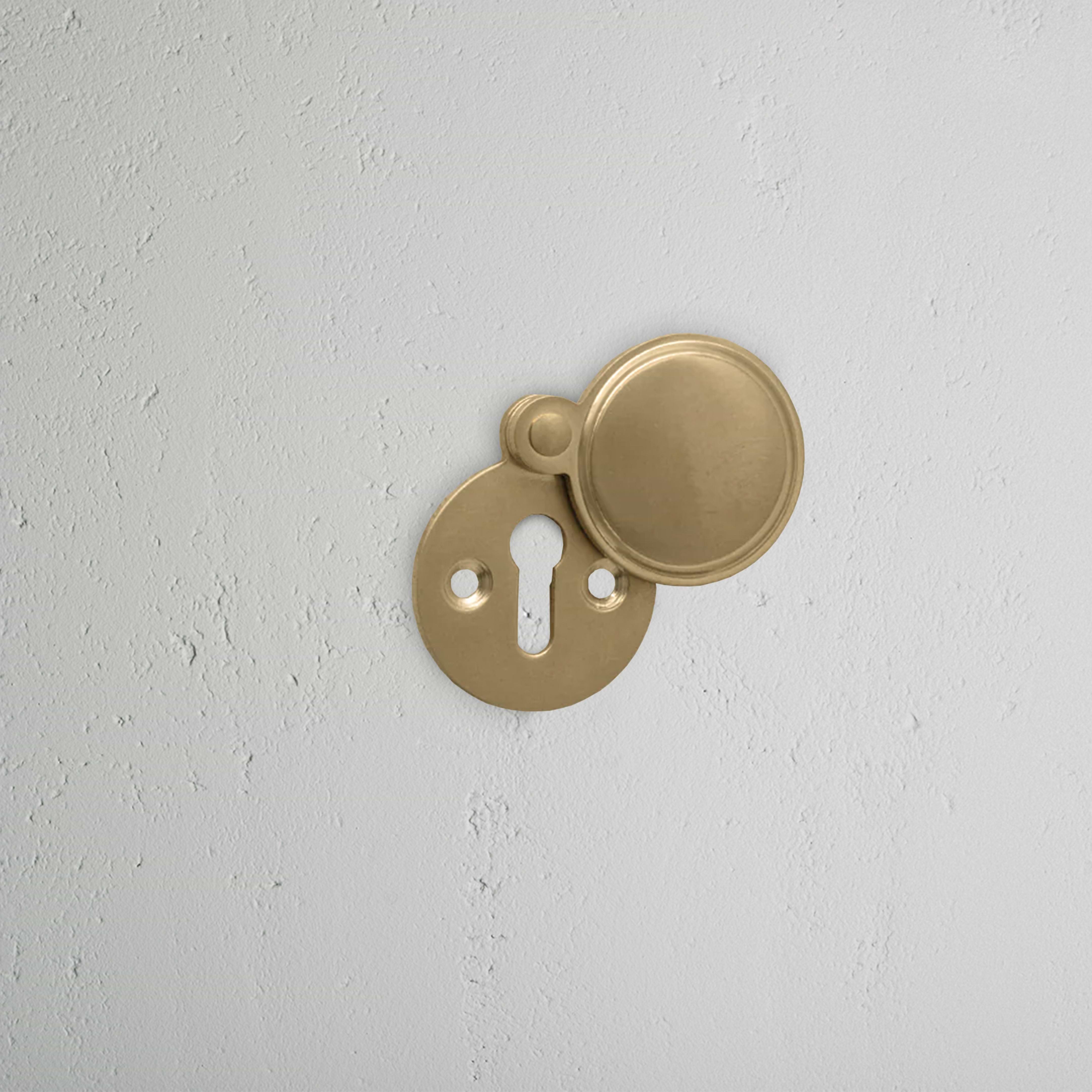 Warwick Covered Key Escutcheon in Antique Brass with round cover, partially open to show keyhole.
