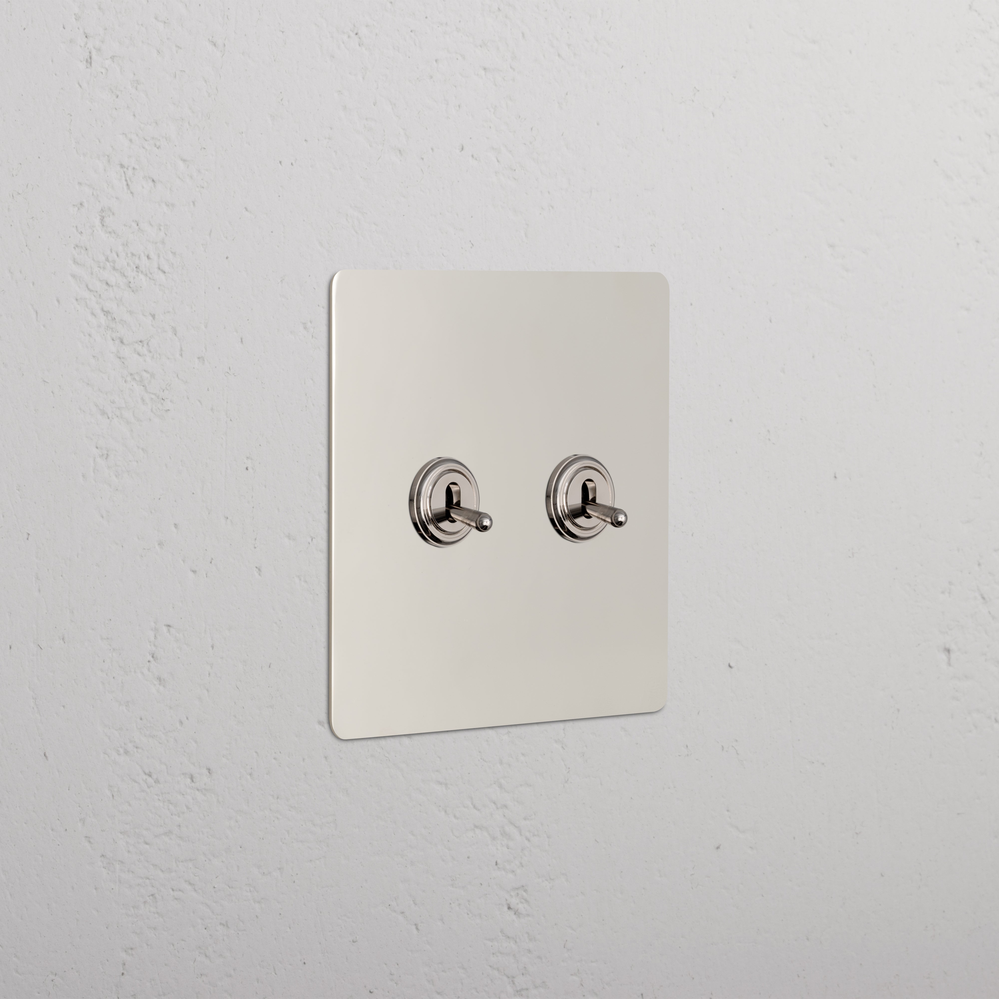 Kew 2G Toggle Switch in polished nickel with two toggle switches on a metallic plate, mounted on a wall.