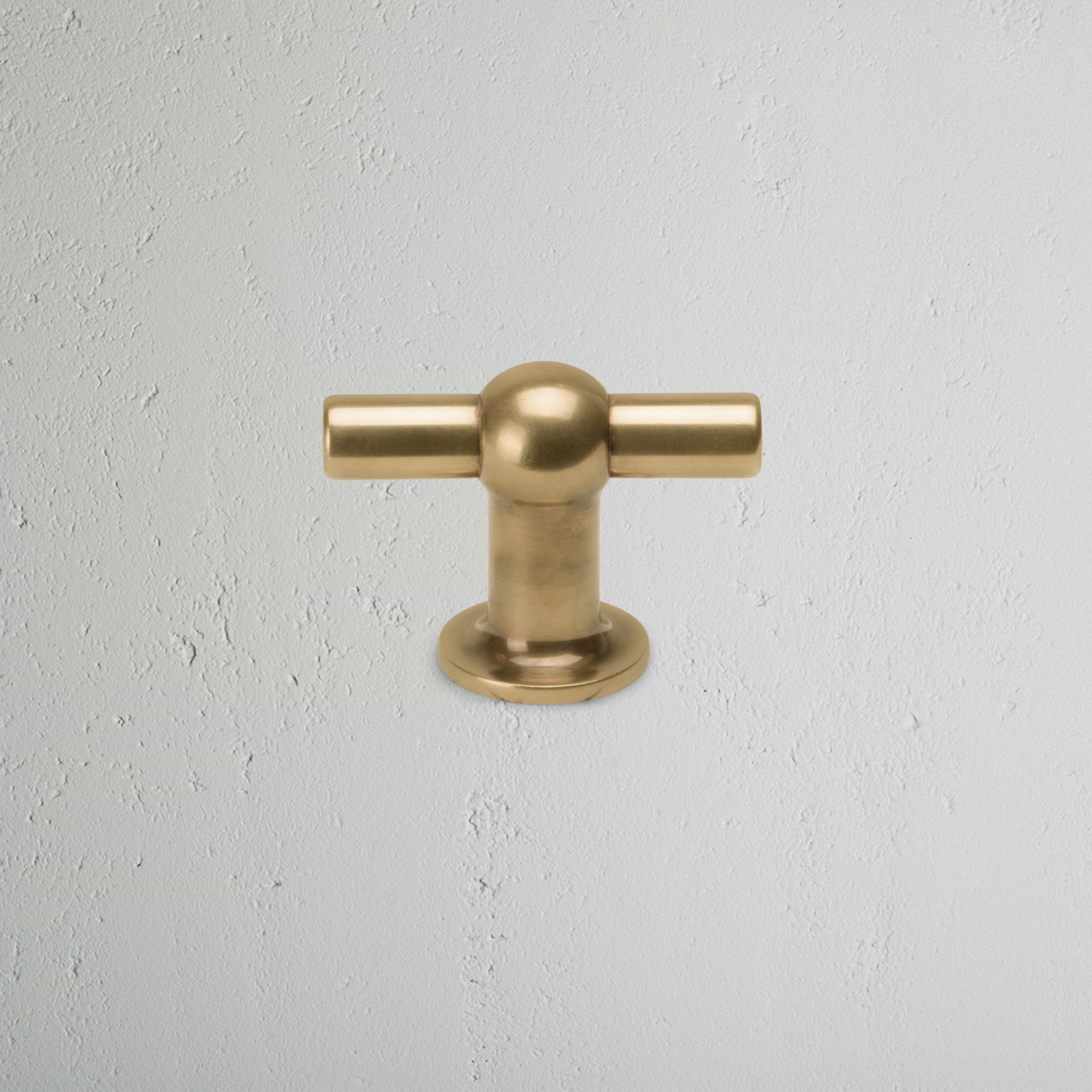 Harper T-Bar Furniture Handle Medium in antique brass, T-shaped, mounted on a light gray textured surface.