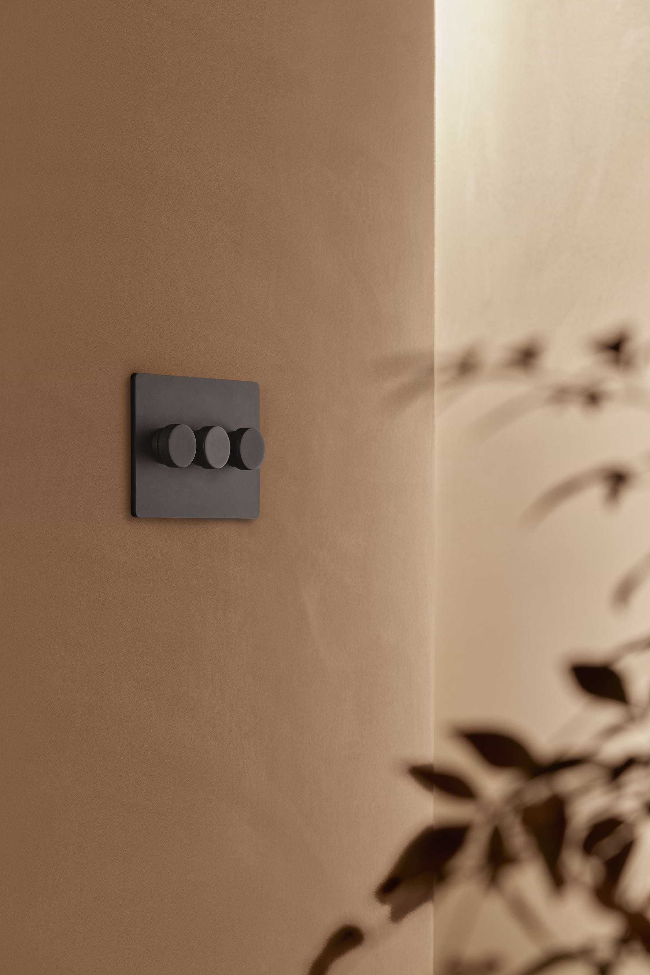 Bronze Grove 3G Dimmer Switch mounted on a beige wall, with soft shadows creating a modern look.