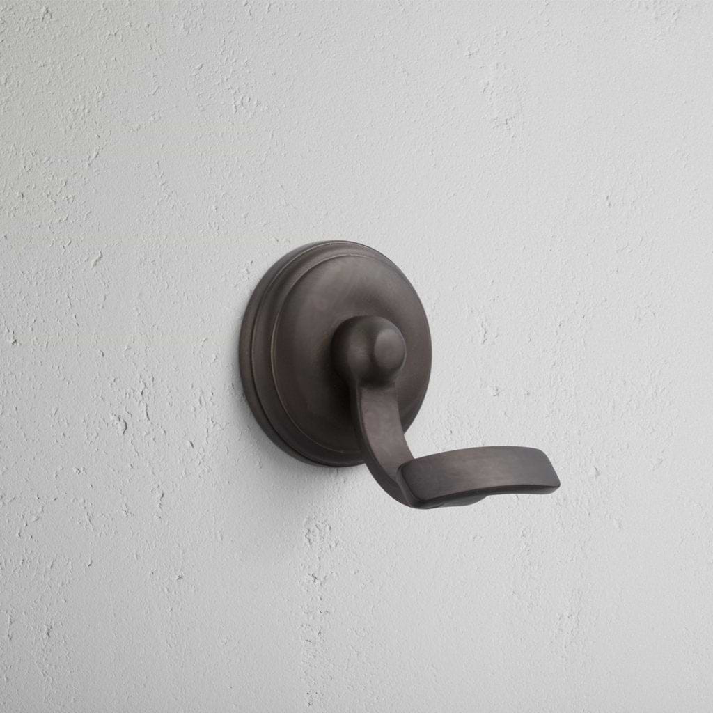 Portland Hook in bronze finish, featuring a curved design, mounted on a light grey textured wall.