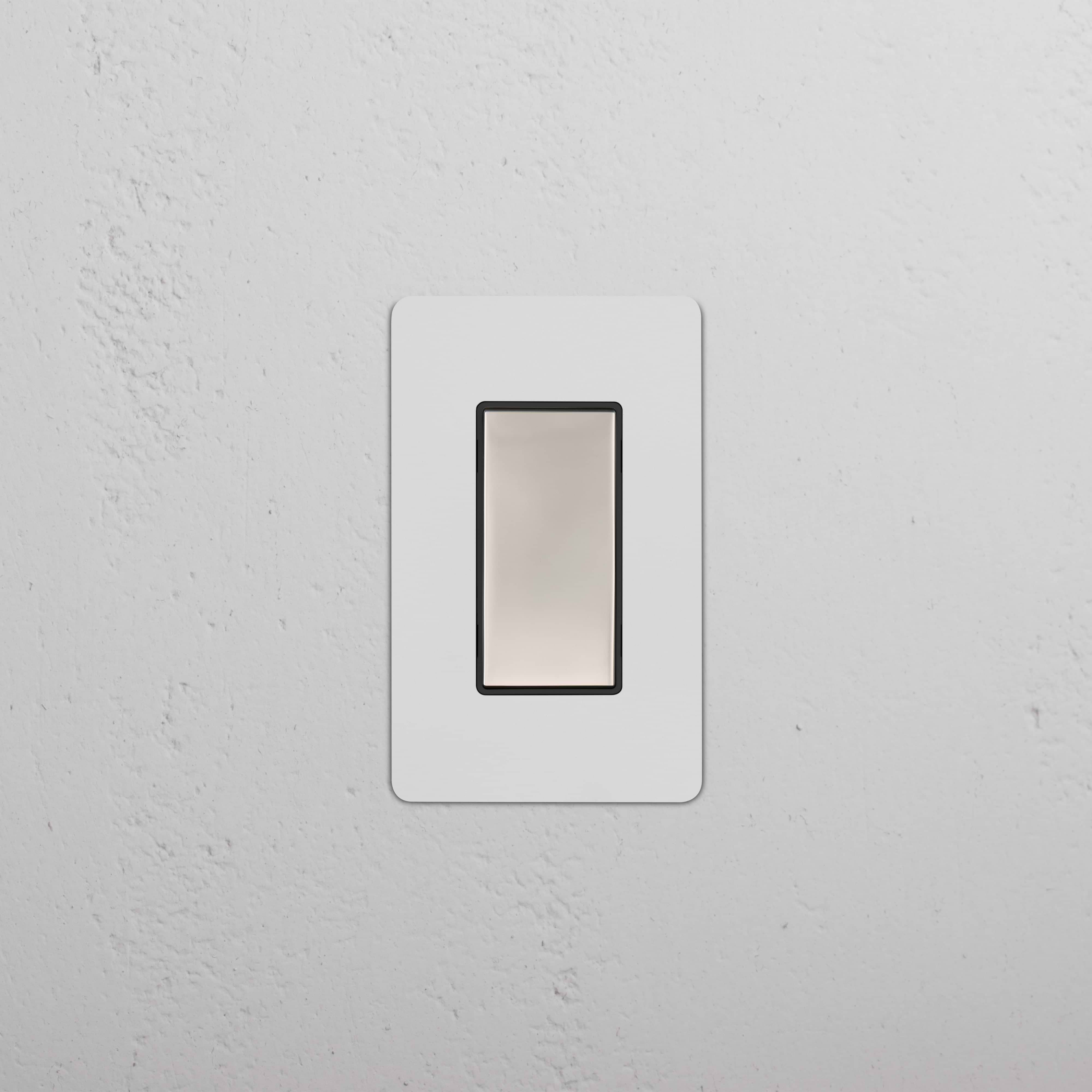 Kew 1G Center Retractive Rocker Switch in Paintable Polished Nickel Black, shown mounted on a white wall.