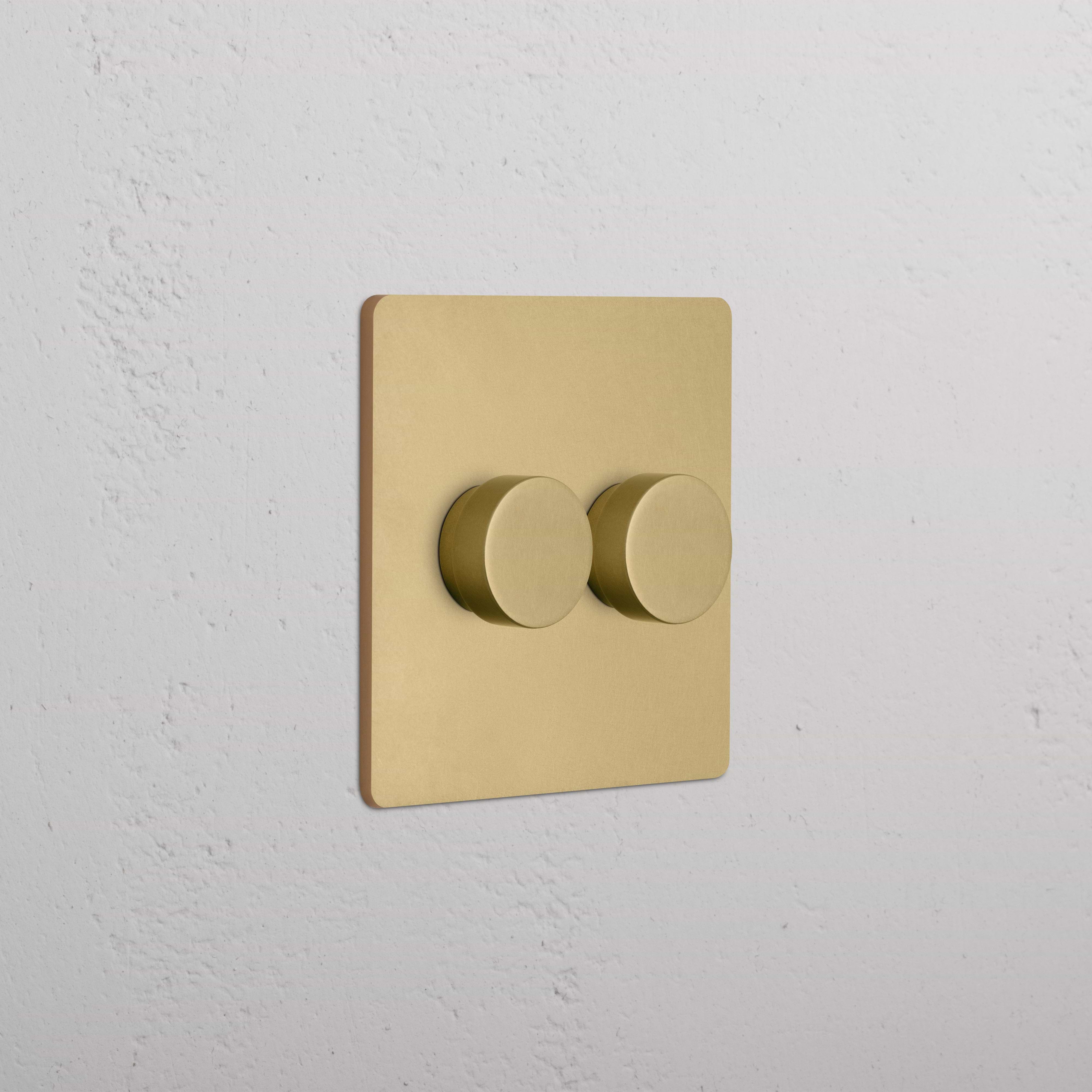 Grove 2G Dimmer Switch in Antique Brass with two round knobs on a square plate, mounted on a wall.