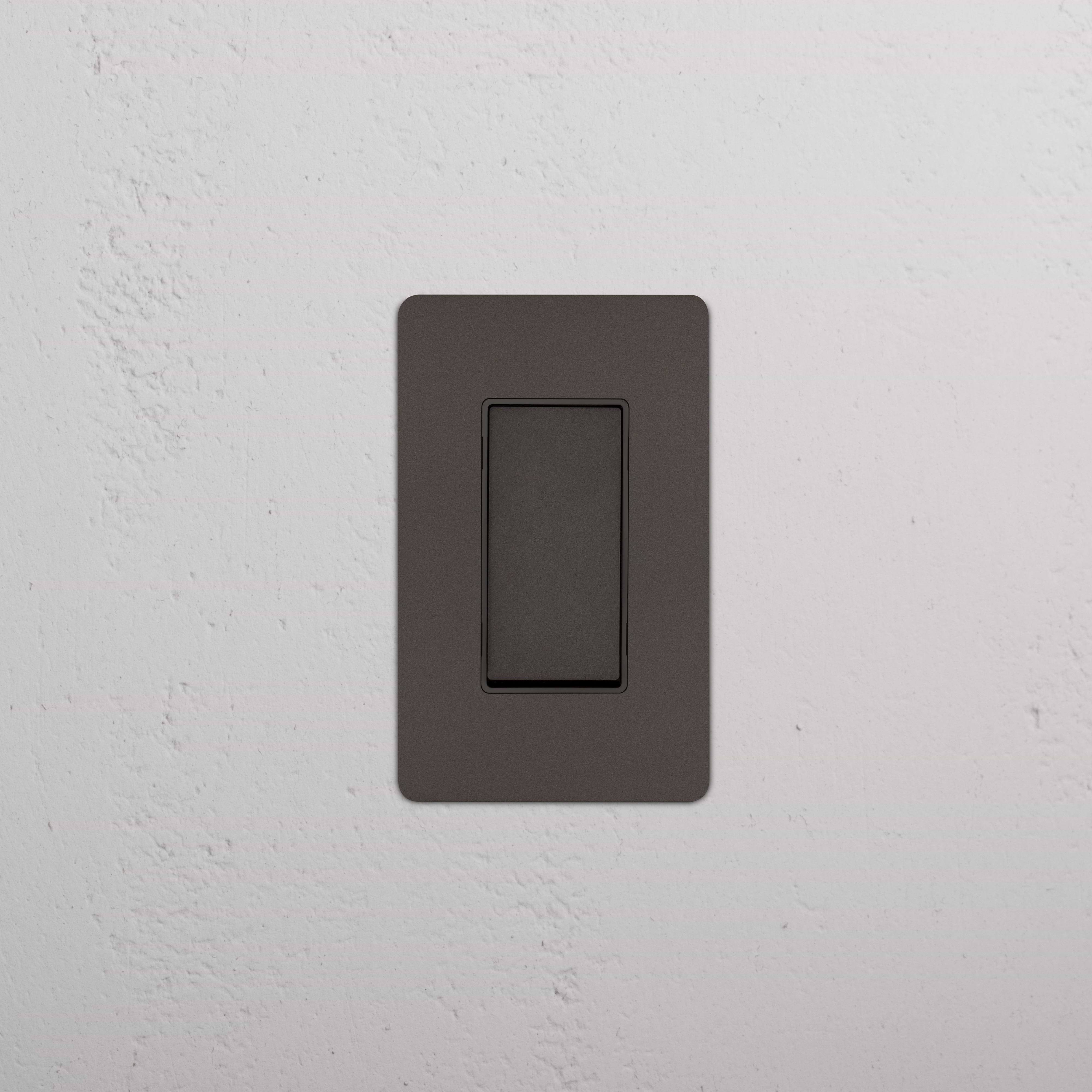 Kew 1G Four Way Rocker Switch in Bronze Black with matching plate, installed on a white textured wall.