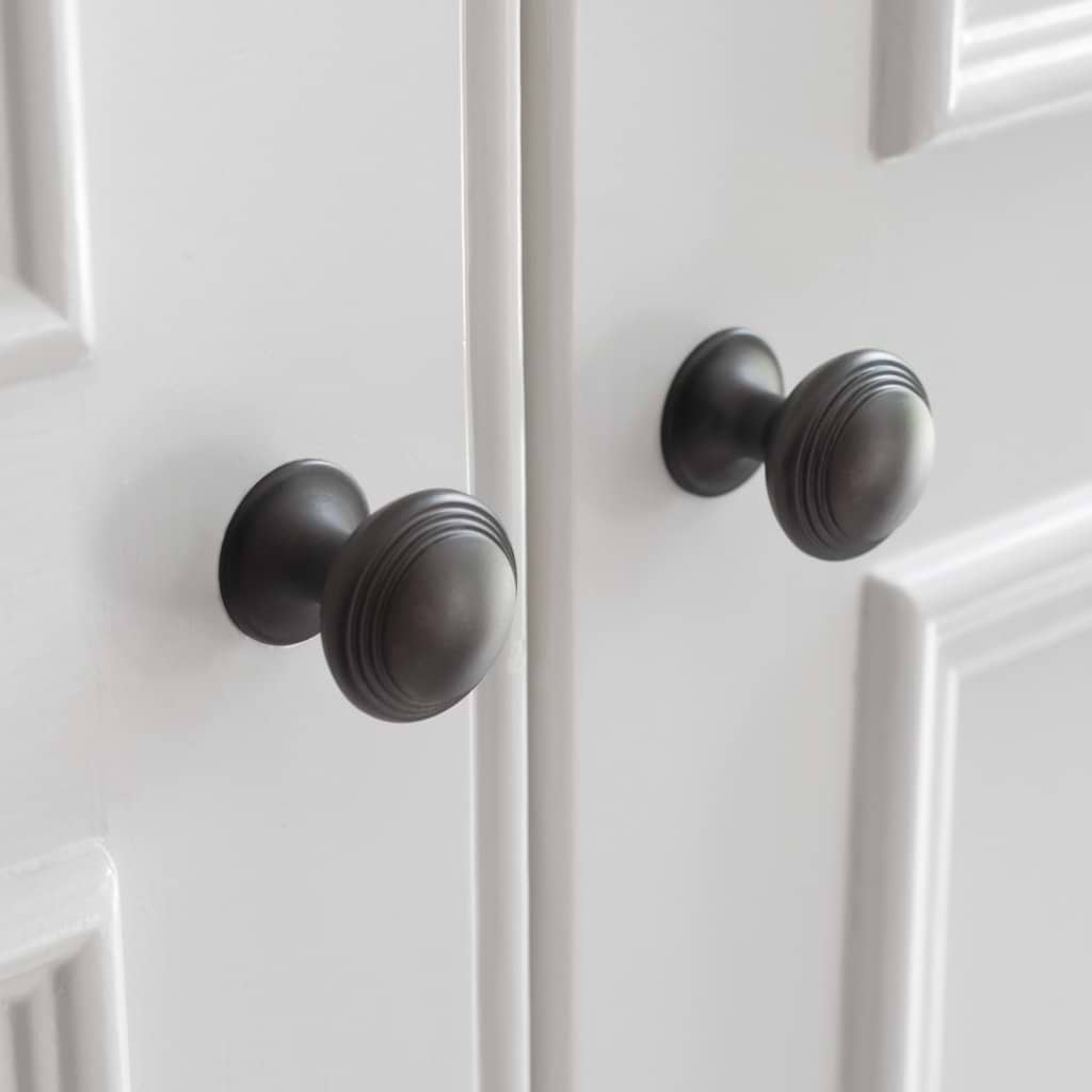 Close-up of two Barlow Furniture Knob Small - Bronze knobs with a ribbed design on white paneled doors.