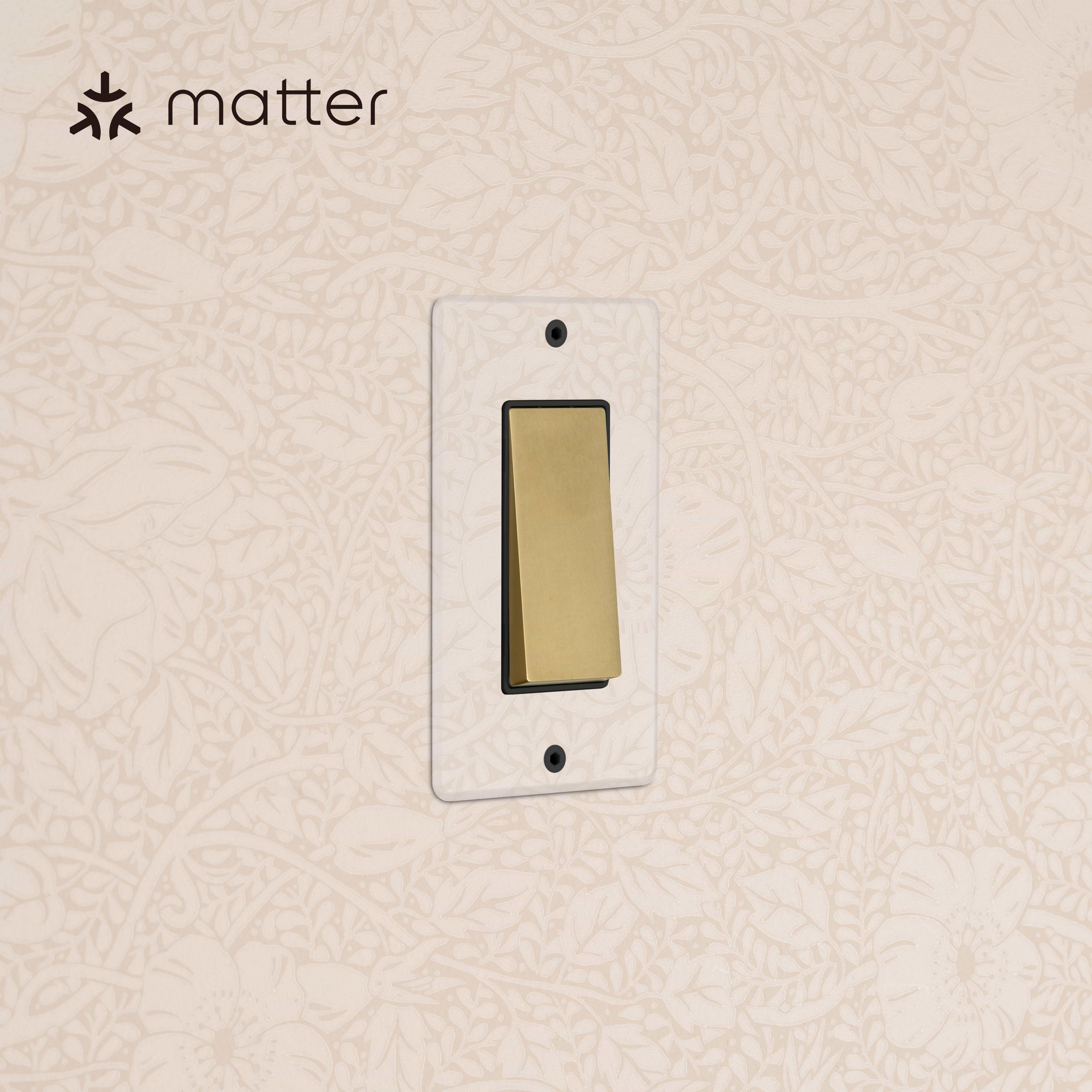 Kew 1G Smart Retractive Rocker Switch in clear antique brass with black trim, mounted on floral-pattern wallpaper.