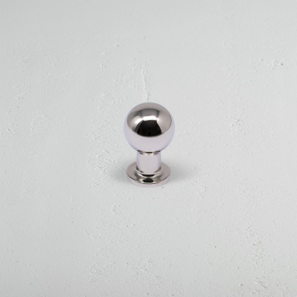 Small polished nickel Bayswater furniture knob with spherical head and short base on a light gray surface.