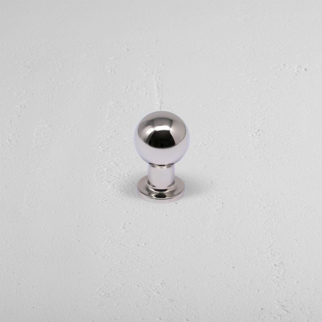 Small polished nickel Bayswater furniture knob with spherical head and short base on a light gray surface.